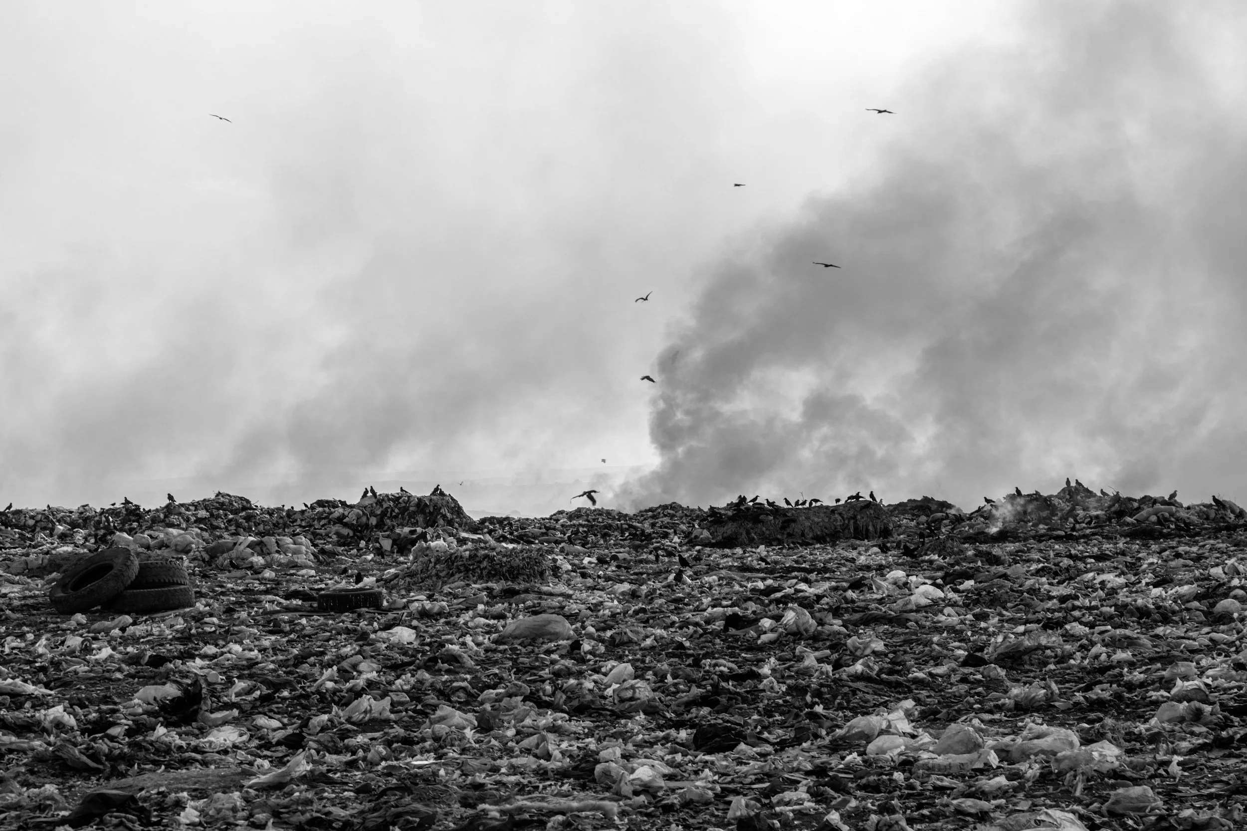 A landfill or dump filled with trash and debris, with tires in the foreground and dark clouds in the sky.