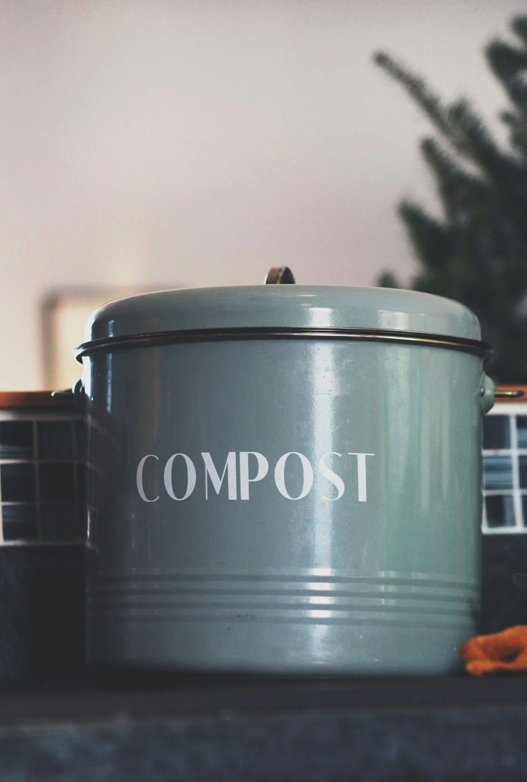 A gray compost bin with the word 'COMPOST' written in white on the front, placed on a countertop.