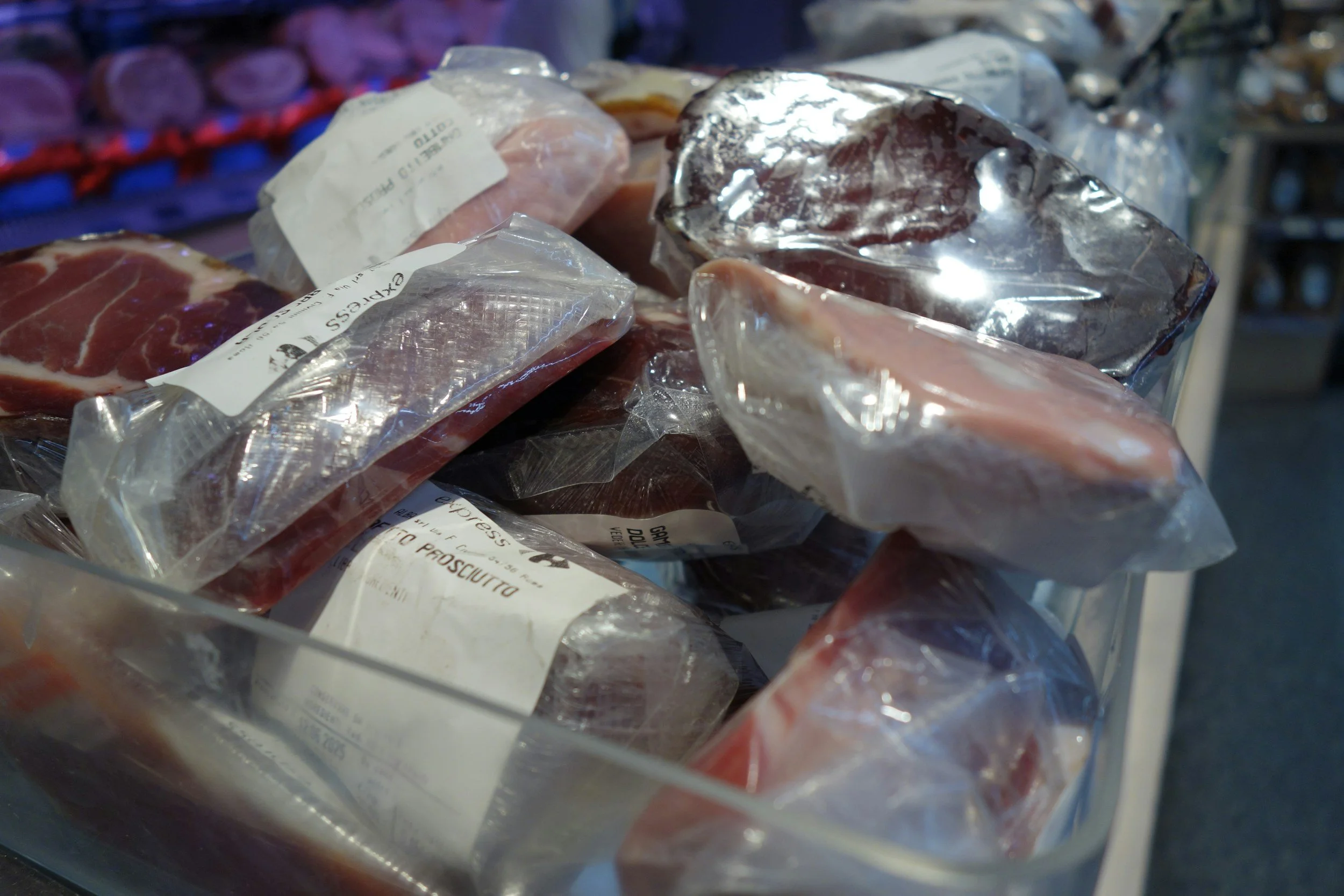 Various cuts of raw meat packaged in plastic, on a refrigerated shelf in a grocery store.