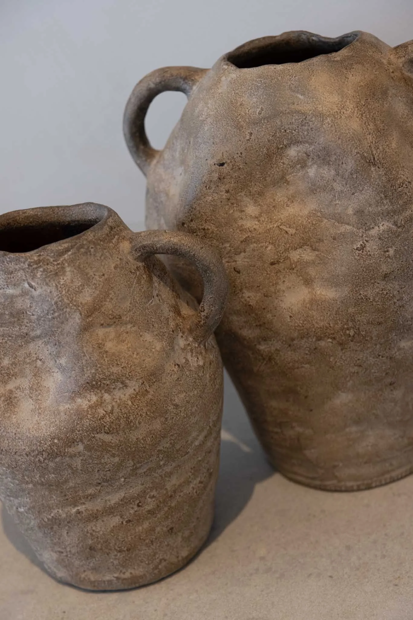 Close-up of three worn, beige clay pottery vessels with small handles, placed on a flat surface against a plain background.