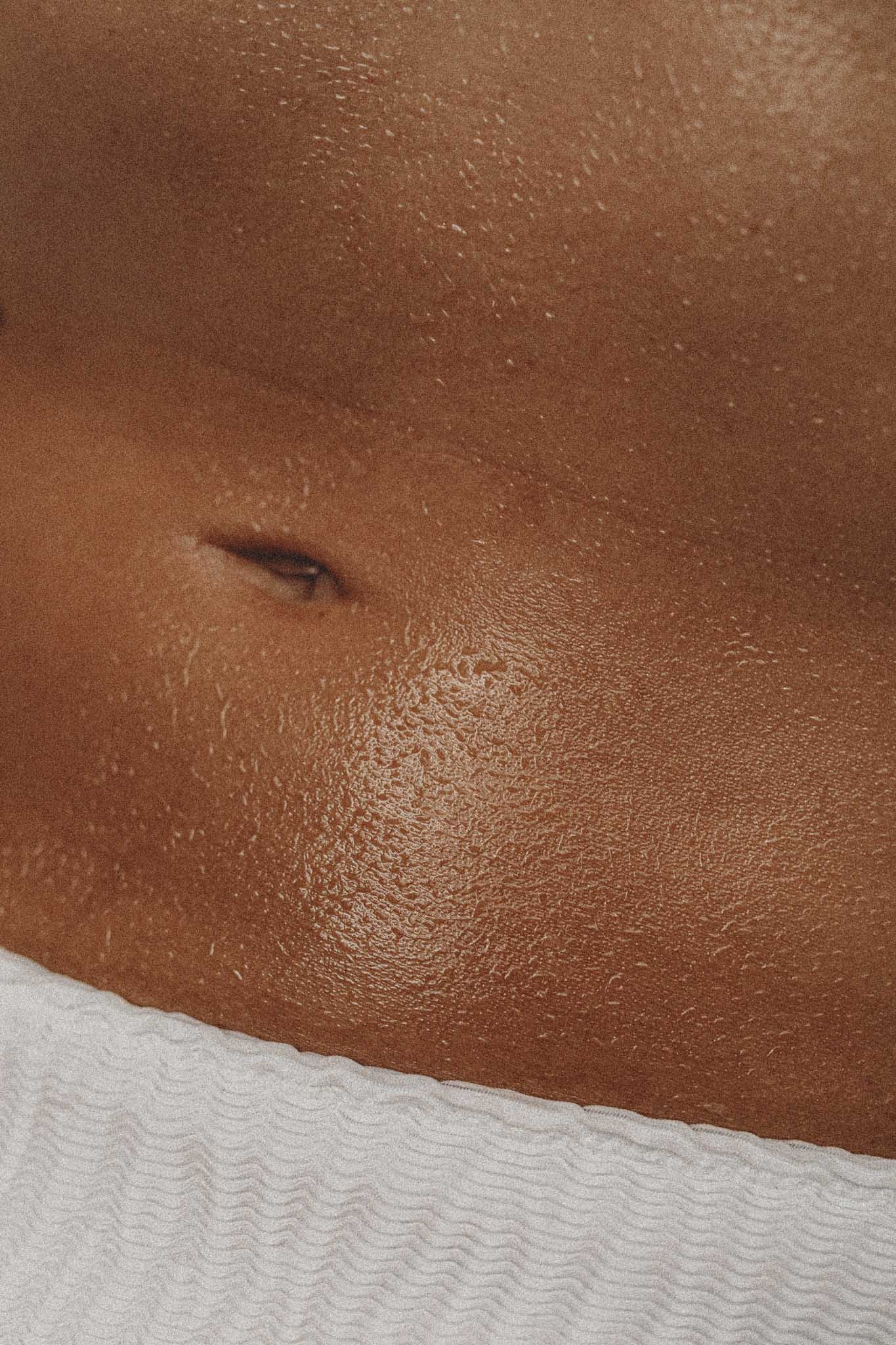 Close-up of a person's abdomen showing skin and a navel, with a white textured fabric at the bottom.