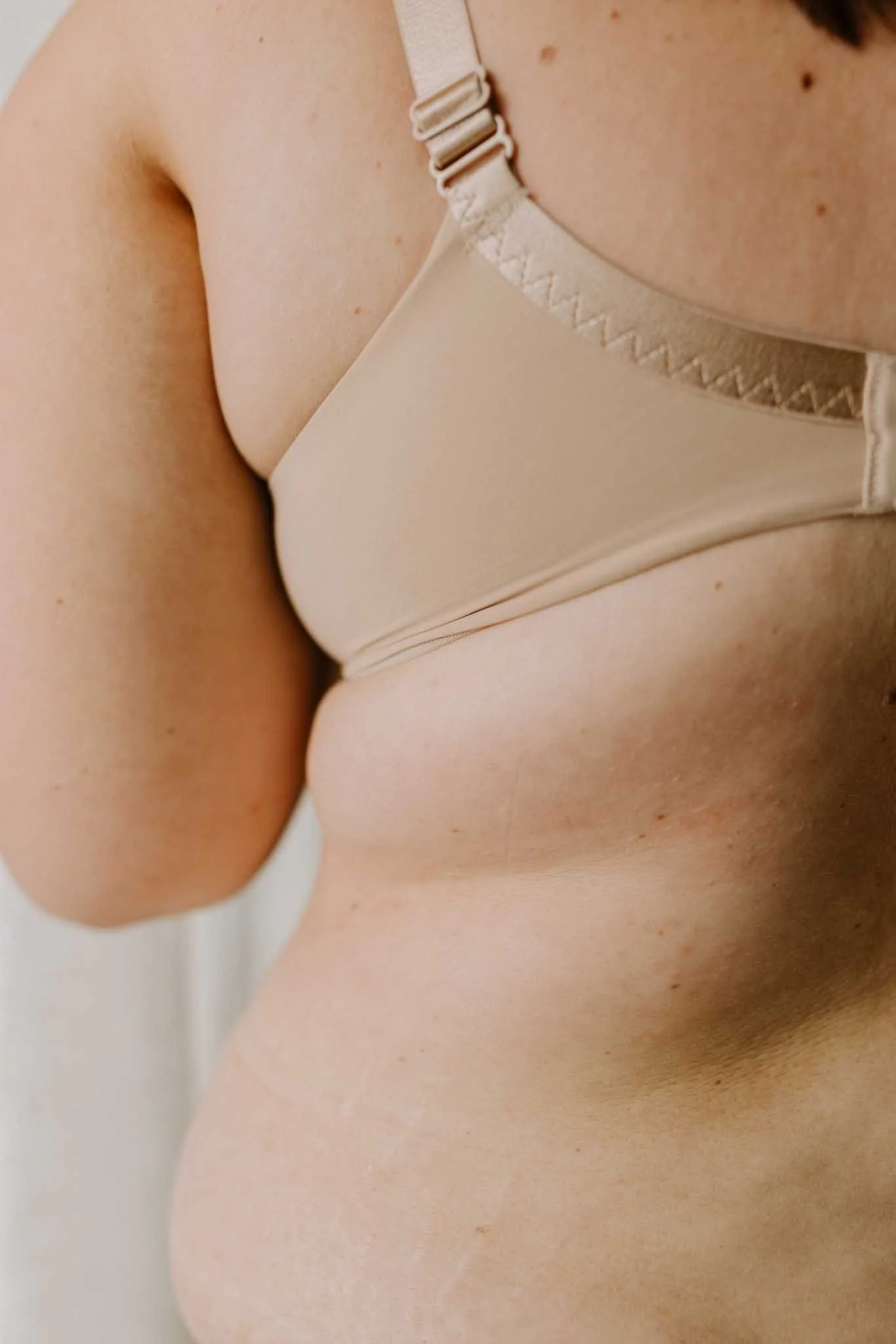 Close-up of a woman's shoulder, part of her neck and her upper arm, wearing a beige bra with a strap visible.