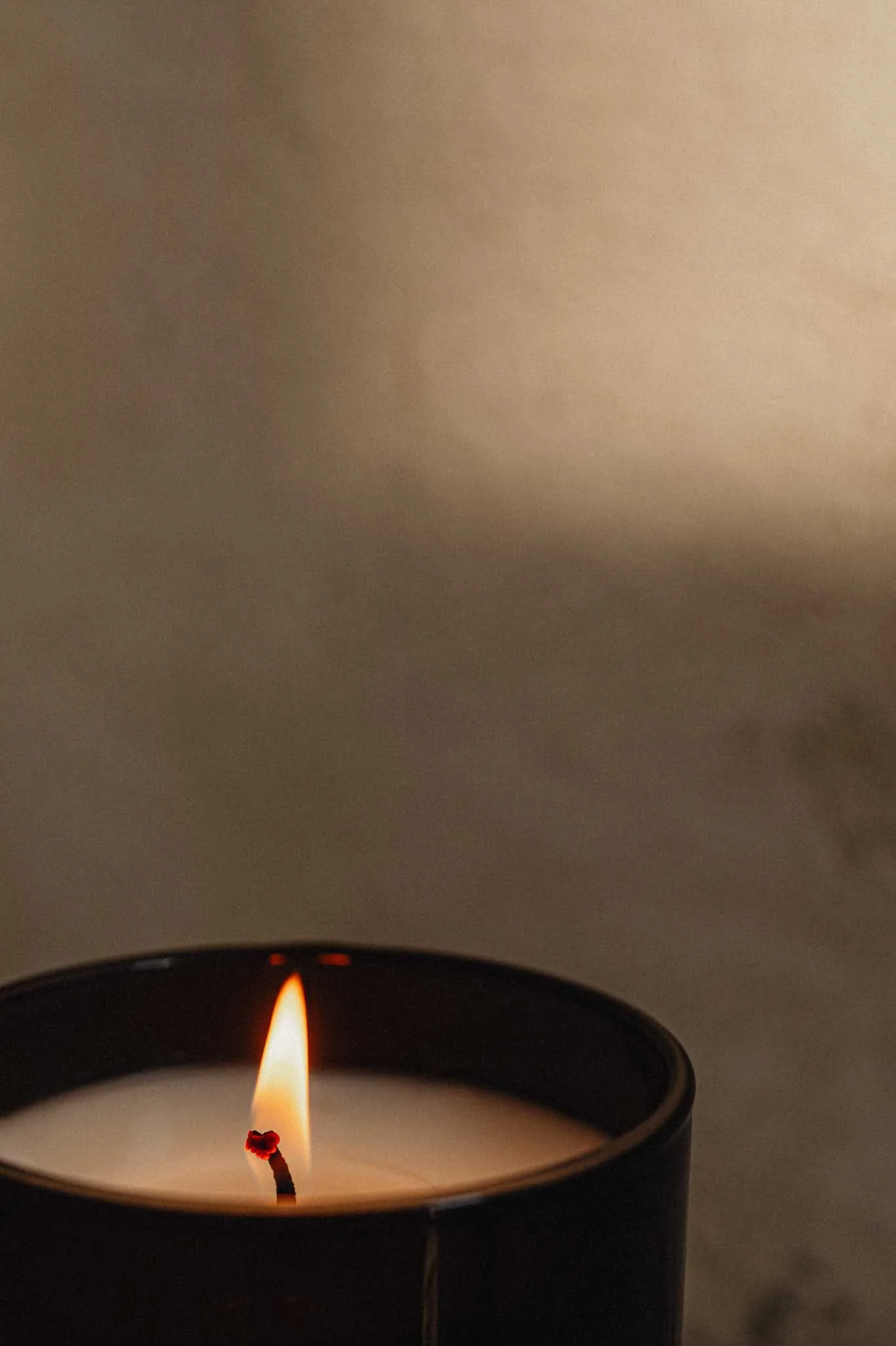 A burning tealight candle in a black container with a small flame and a slightly melted wick.