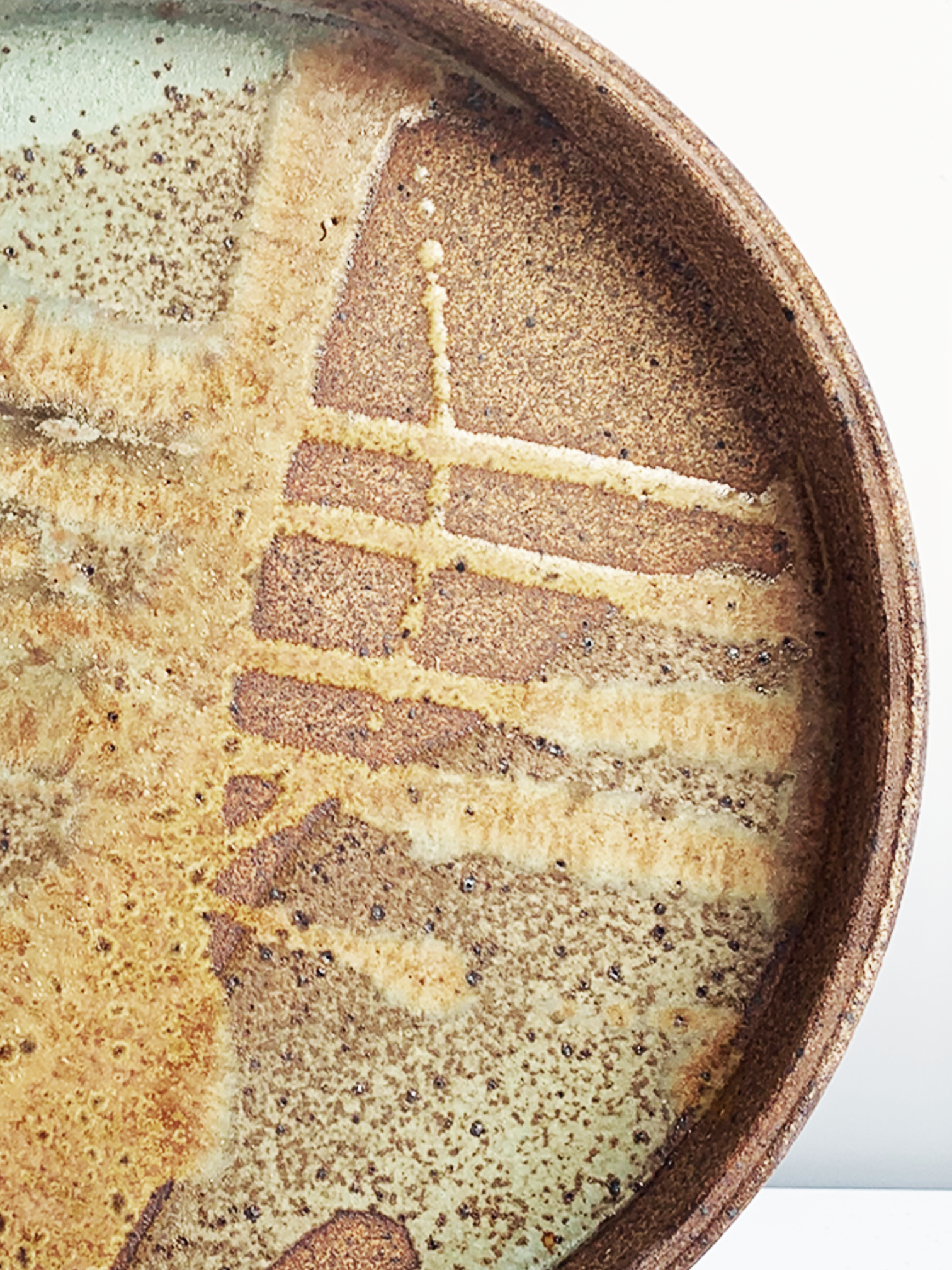 Handmade round stoneware platter with a brown clay rim and layered turquoise, tan, and brown glazed interior.