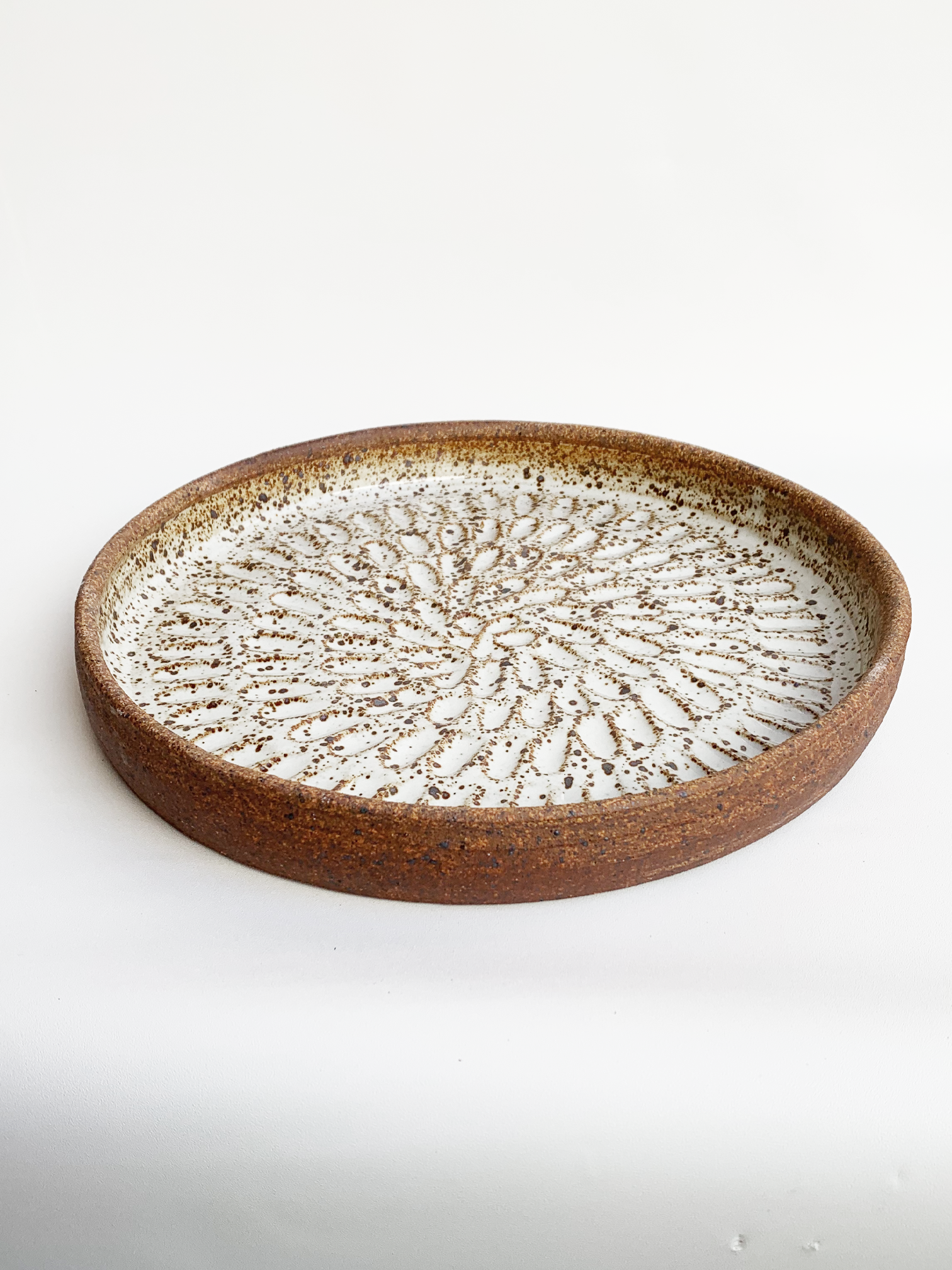 Handmade stoneware platter with a warm brown clay rim, glossy white glazed interior, and carved radiating pattern.