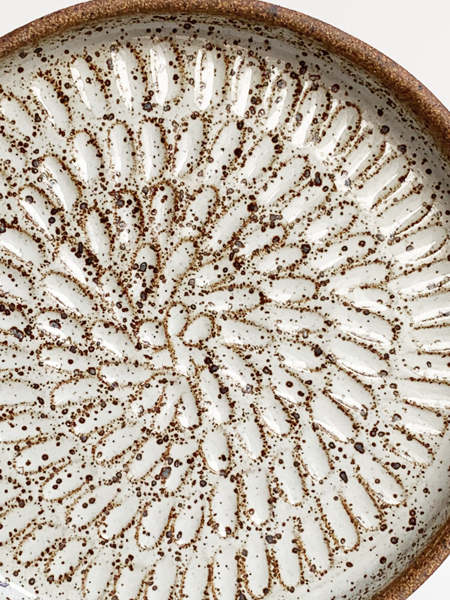 Handmade stoneware platter with a warm brown clay rim, glossy white glazed interior, and carved radiating pattern.