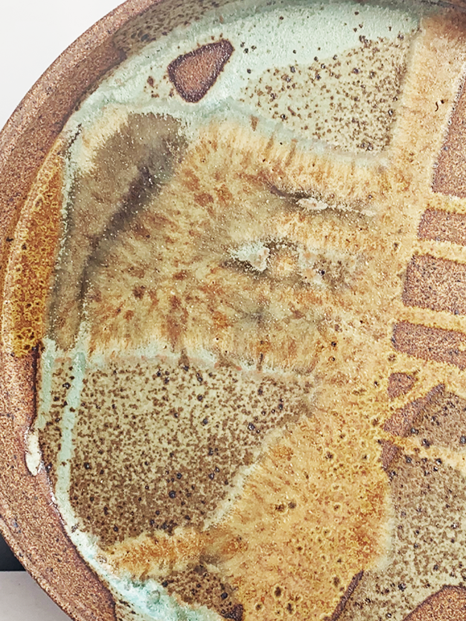 Handmade round stoneware platter with a brown clay rim and layered turquoise, tan, and brown glazed interior.