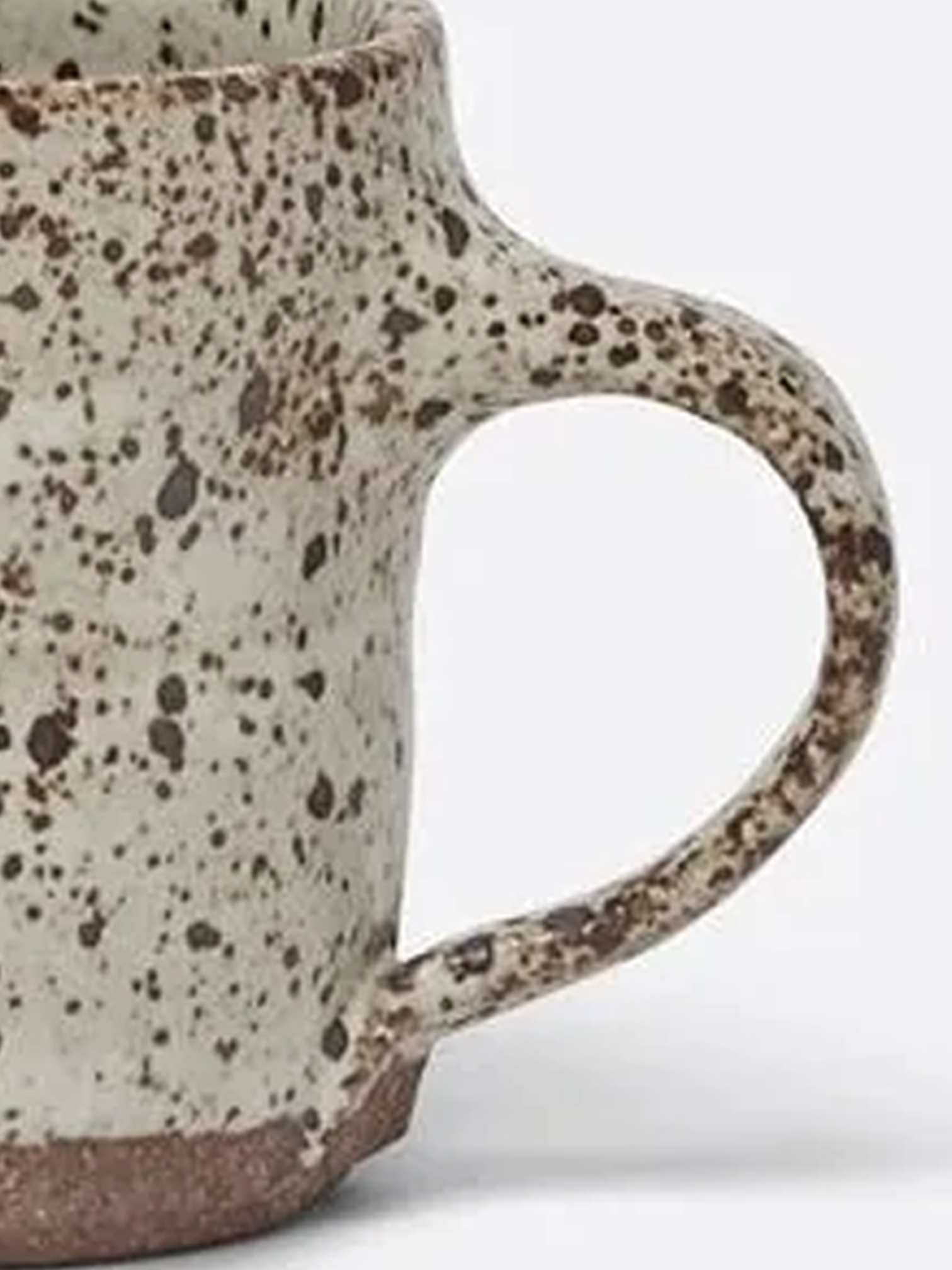 Handmade cylindrical stoneware mug with a pale speckled glaze, exposed brown clay base, and rounded handle.