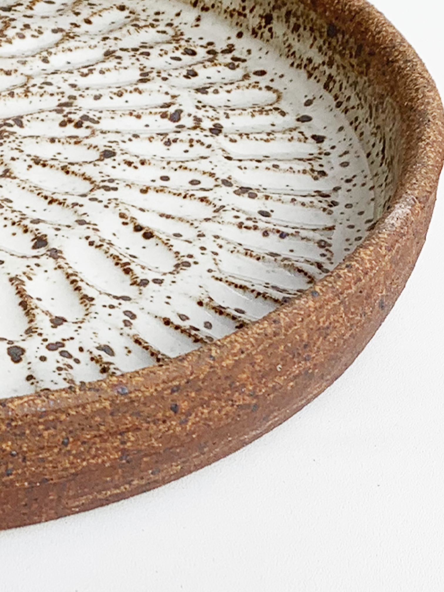 Handmade stoneware platter with a warm brown clay rim, glossy white glazed interior, and carved radiating pattern.