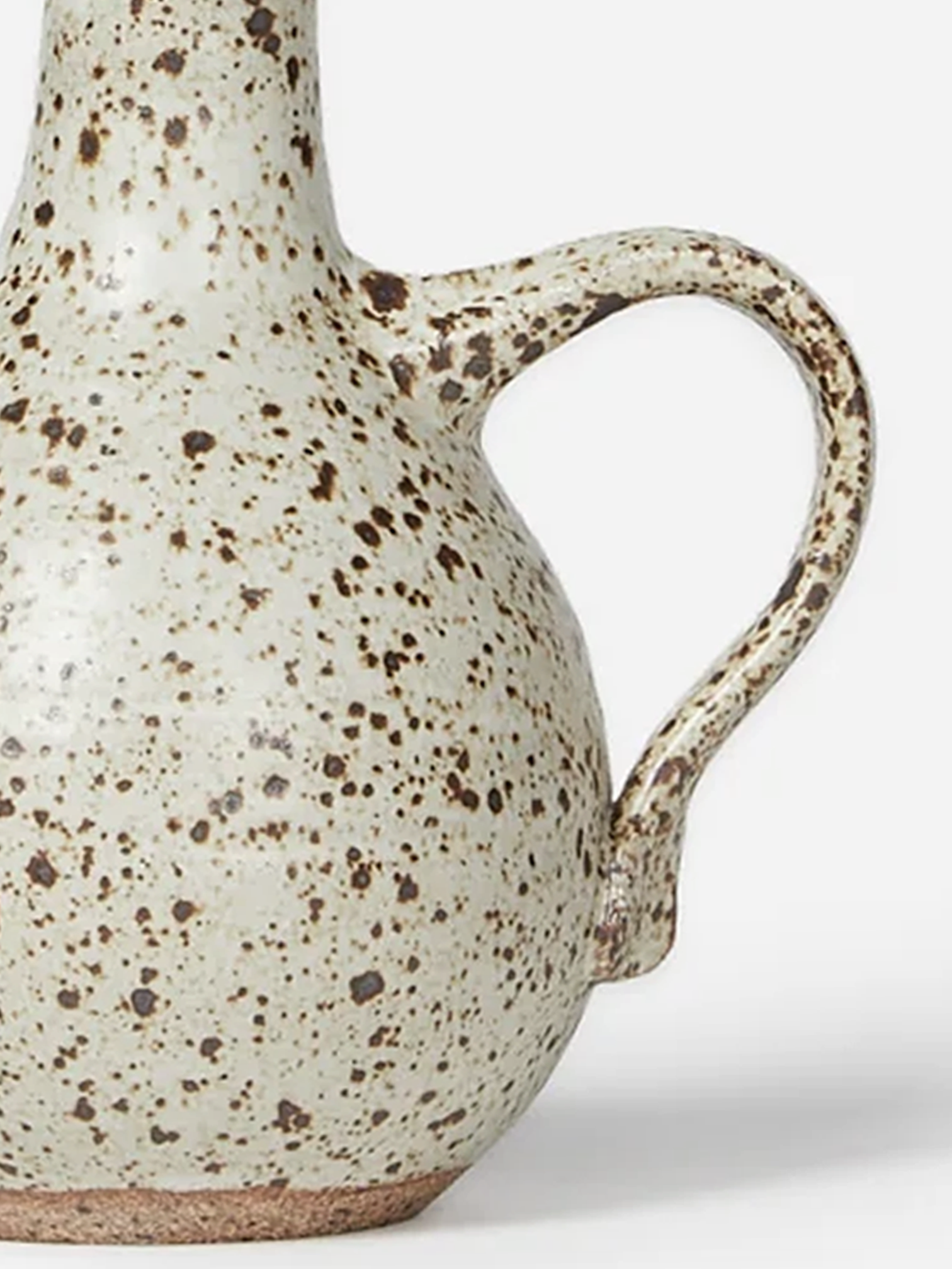 Handmade stoneware oil cruet with a pale speckled glaze, rounded body, curved handle, and metal weighted pouring spout.