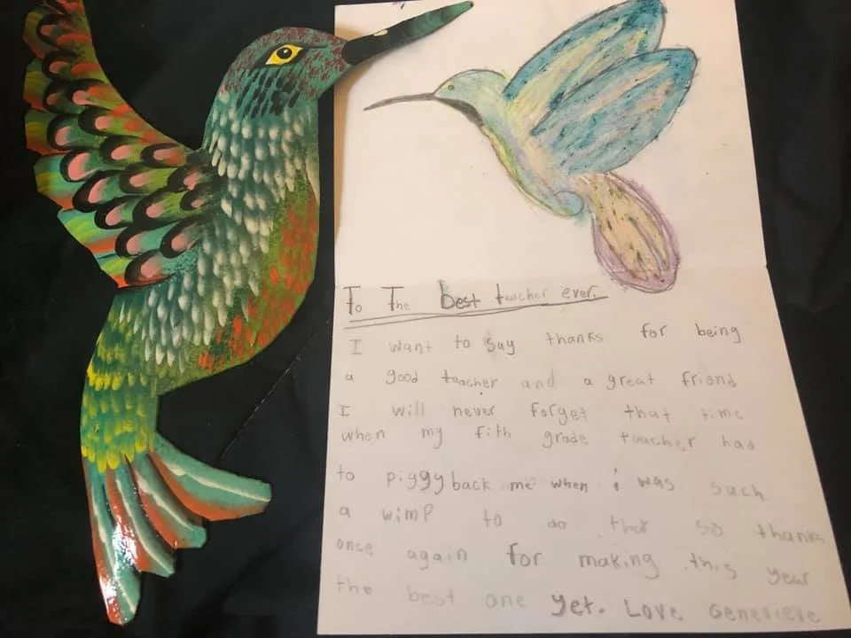 Colorful paper hummingbird cutout and a child's handwritten thank you note to a fifth grade teacher.