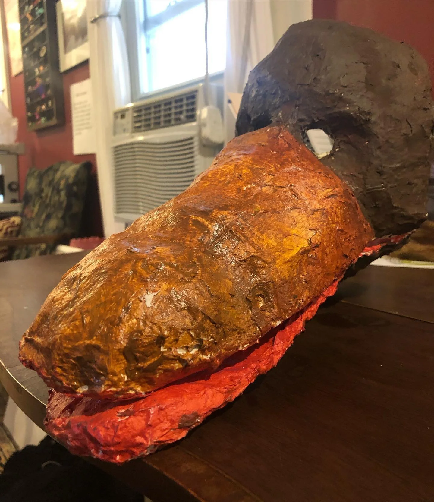 Two large, colorful rocks with a rust-colored one in the foreground and a darker one in the background, placed on a wooden surface inside a room.