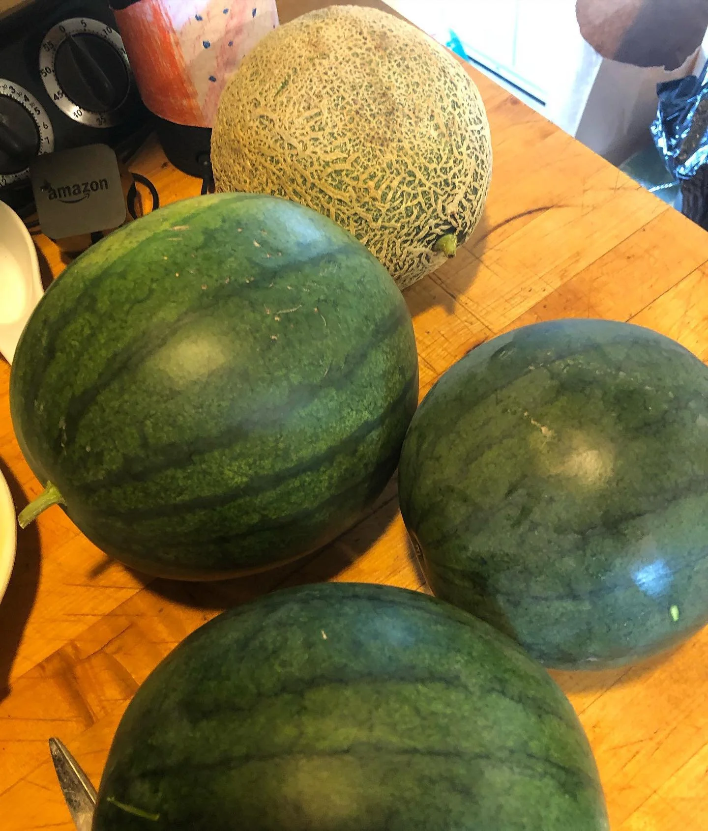 Three watermelons and one cantaloupe on a wooden table.