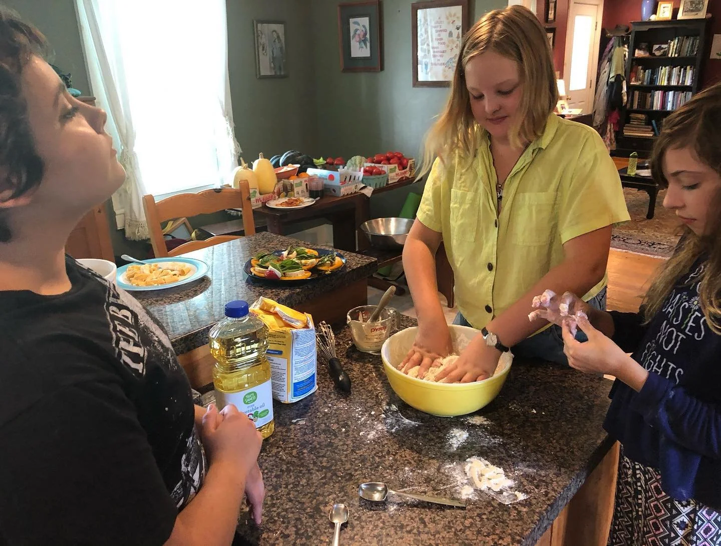 Three children baking together in a kitchen, mixing dough in a large yellow bowl, with various ingredients and utensils on the granite countertop.