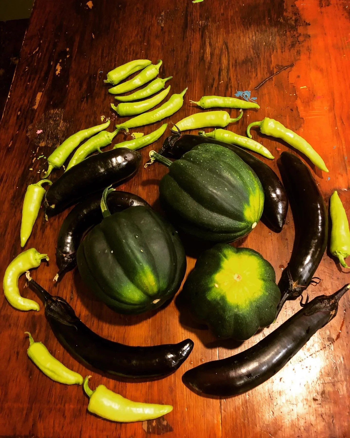 A collection of green and black eggplants and small green peppers arranged on a wooden surface.