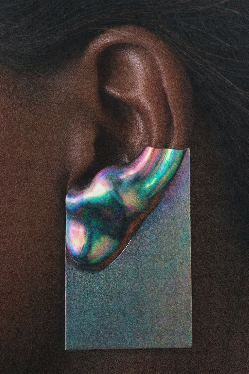 A close-up of a person's ear with a holographic sticker shaped like an ear placed on the earlobe.