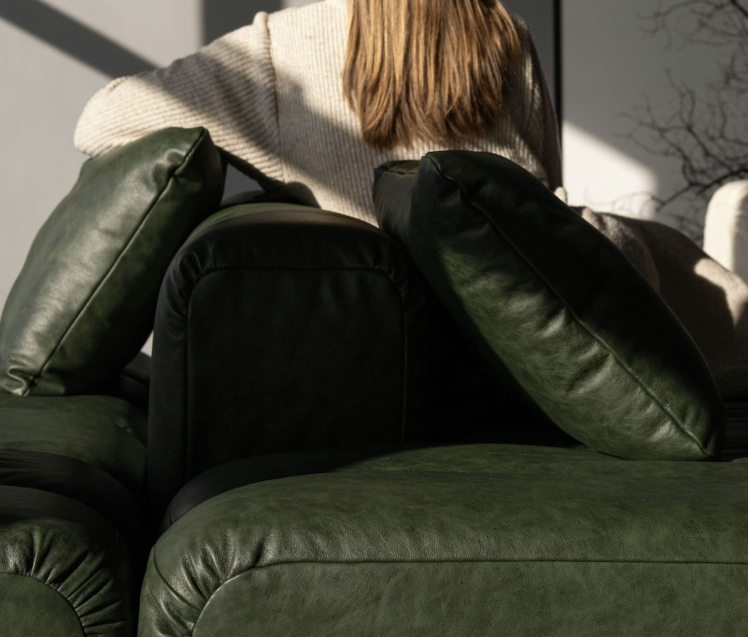 Close-up of a green leather sofa with pillows and a person with brown hair sitting behind it.