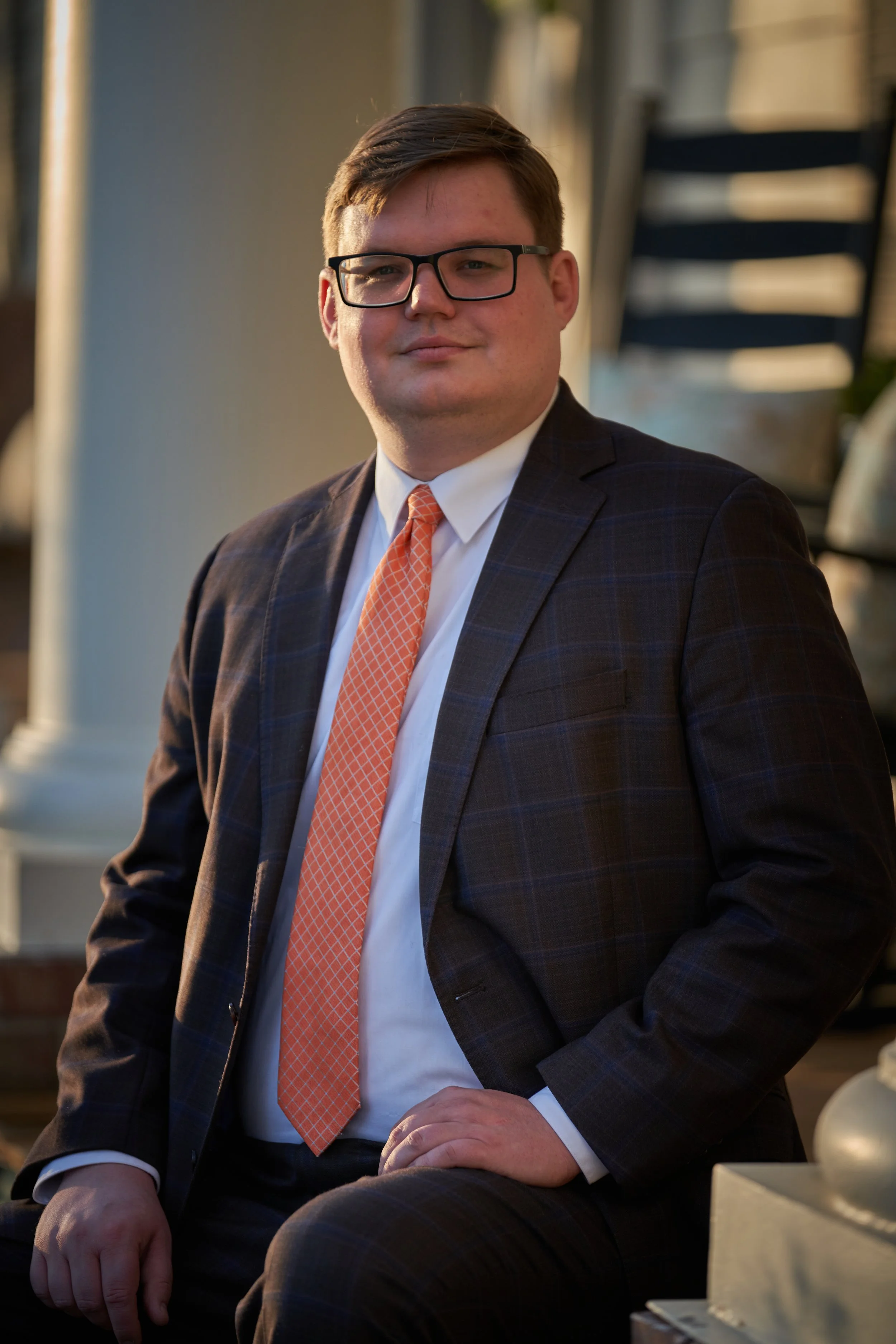 Ryan Harris, Candidate for City Court Judge, a man in a suit and glasses sitting outdoors during sunset, with stairs in the background.