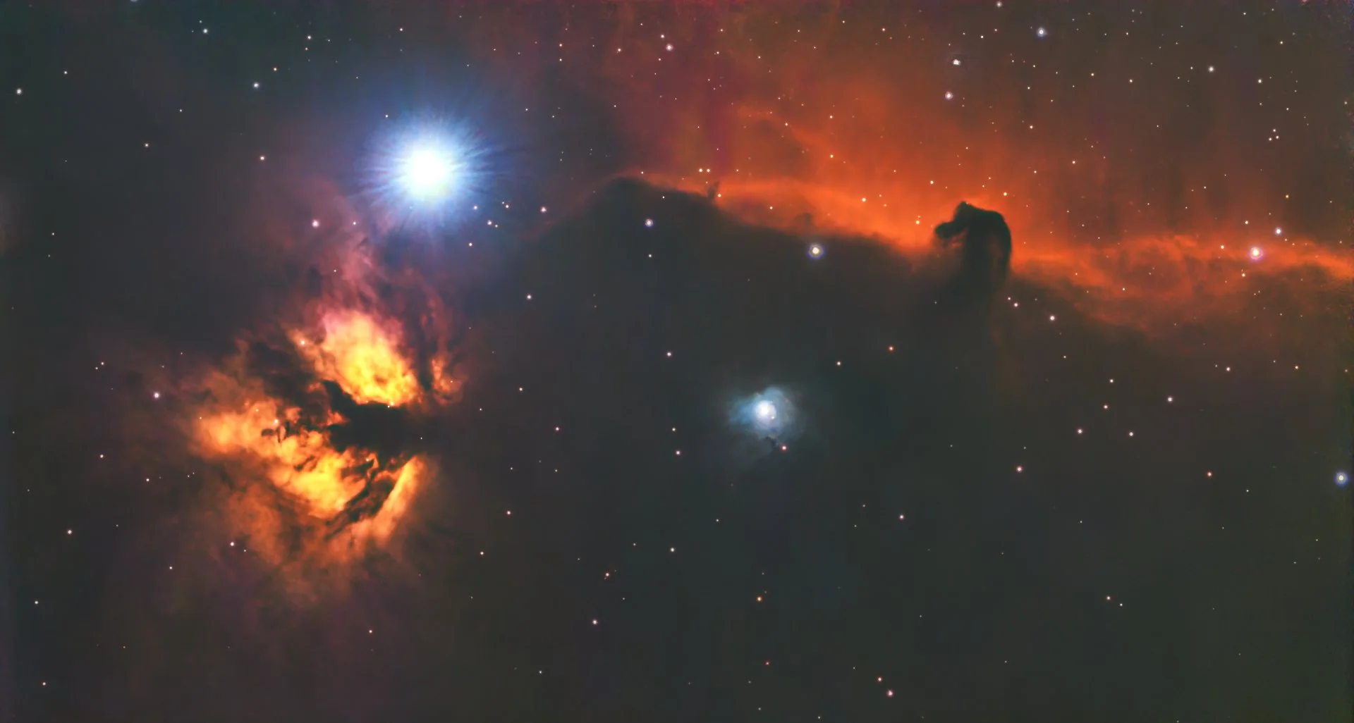 A colorful image of space showing, bright stars, nebulae with orange and red clouds, and a dark silhouette of a horse-shaped figure in the nebula on the right side.