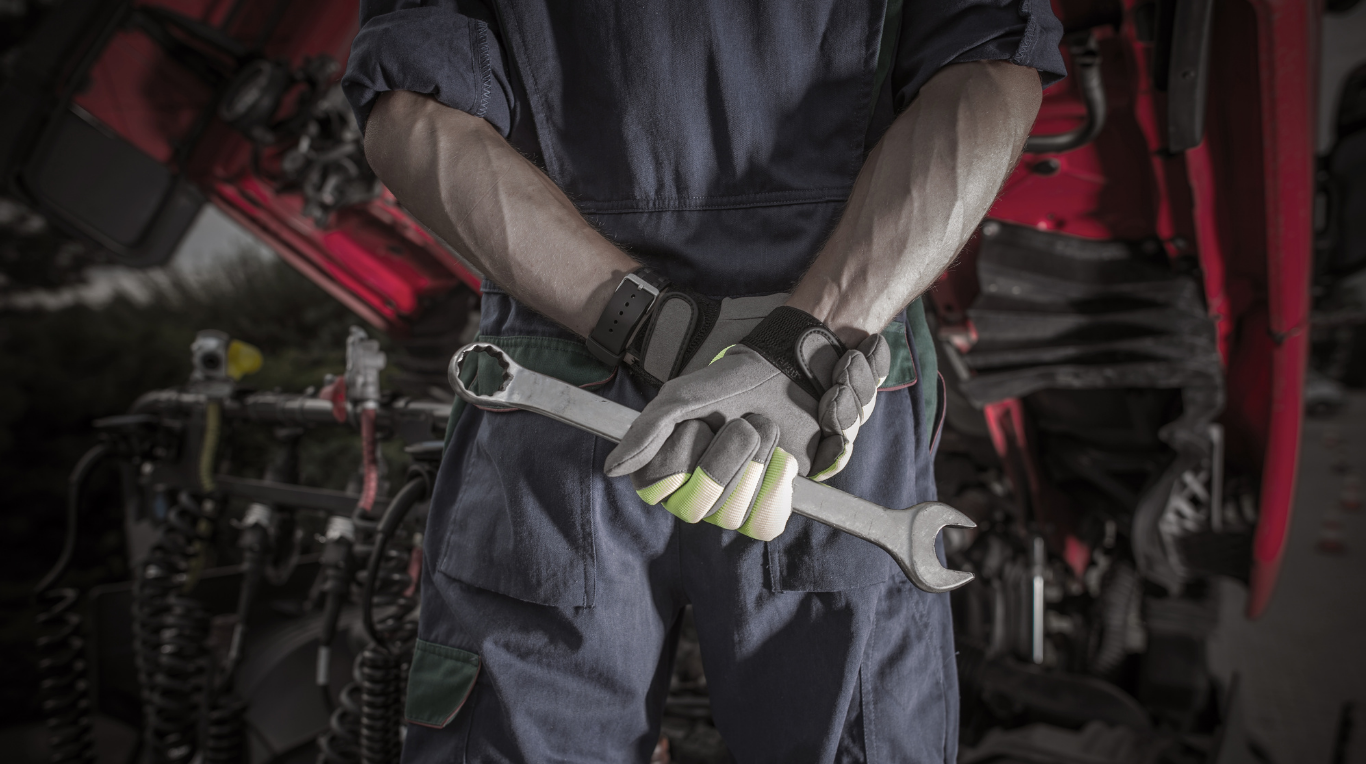 Close-up of a mechanic holding a wrench, wearing gloves, with a red vehicle in the background.
