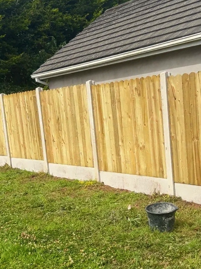 Two men working on a wooden fence outdoors on a sunny day, wearing gloves and using tools.