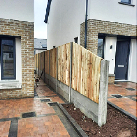 A newly installed wooden privacy fence along a sidewalk between two modern houses.