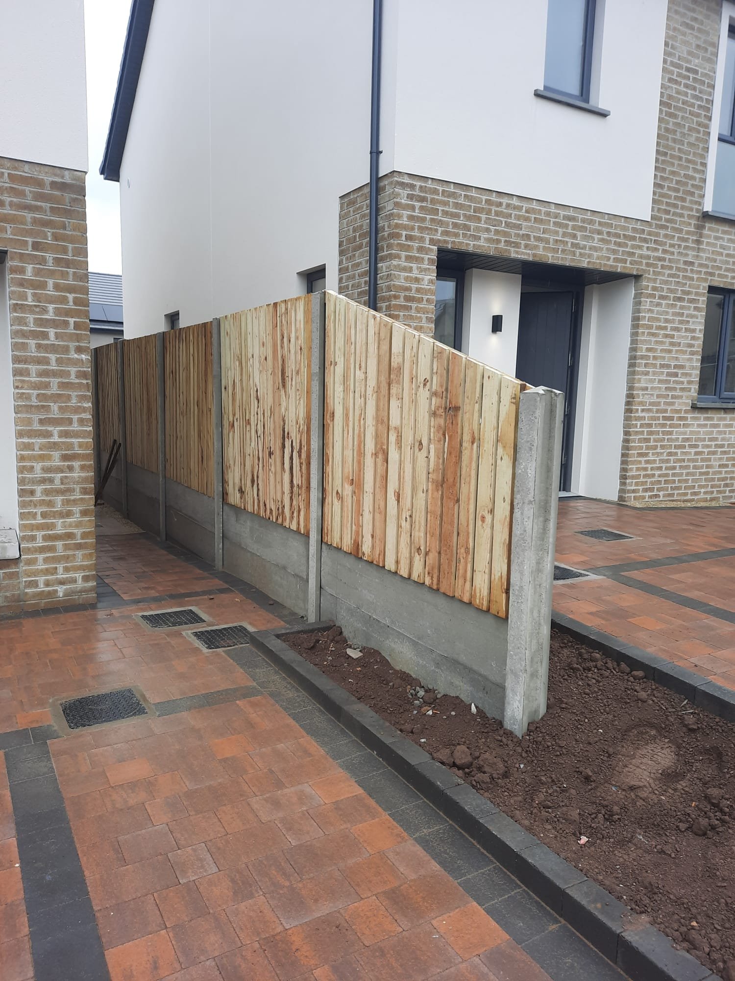 Newly constructed brick townhouse with a small front yard enclosed by a wooden fence and a concrete block foundation, with a paved walkway.