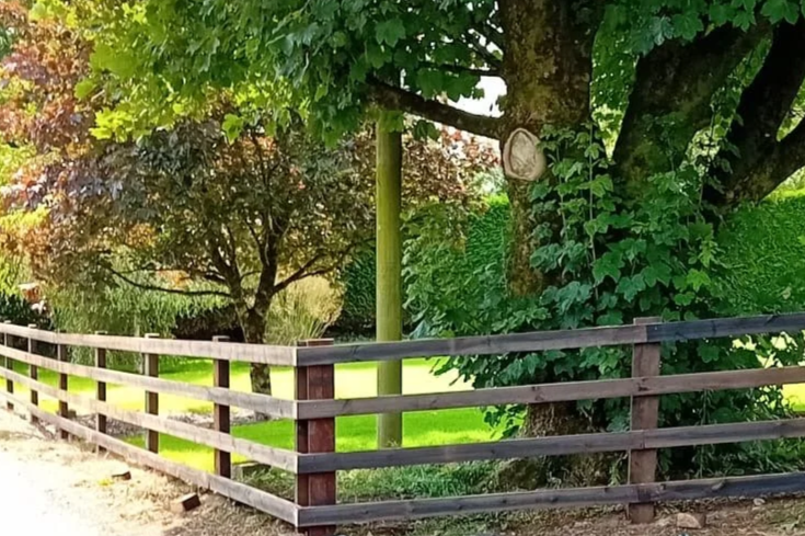 Freshly installed wooden privacy fence with a sidewalk, a house with an awning and solar panels, and a lush green lawn.