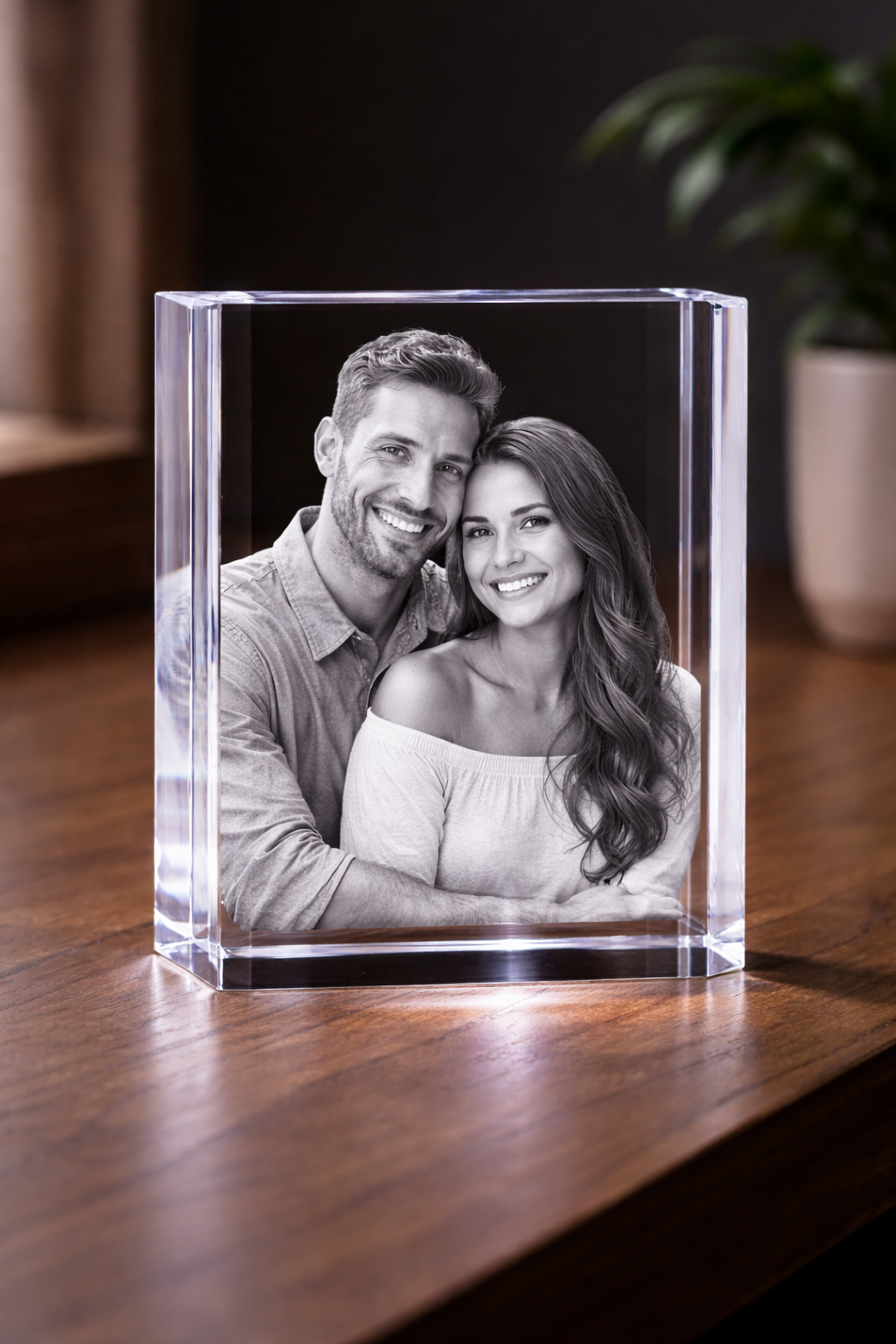 Black and white photo of a smiling young couple inside a clear glass or acrylic frame on a wooden table.