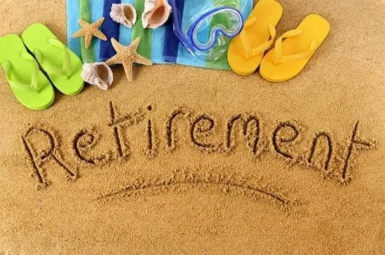 The word 'Retirement' written in the sand at a beach, with colorful flip-flops, starfish, seashells, and a snorkel mask placed nearby.
