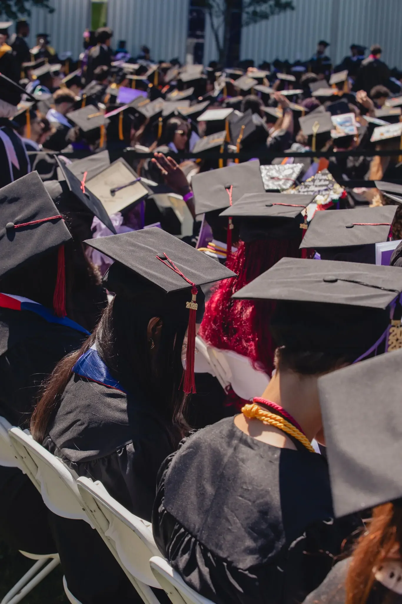 Graduates in caps and gowns seated outdoors at graduation ceremony.