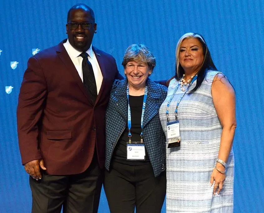 Three professionally dressed individuals smiling and standing together at a formal event with a blue backdrop.