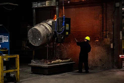 Foundry operator monitoring an industrial melting furnace.