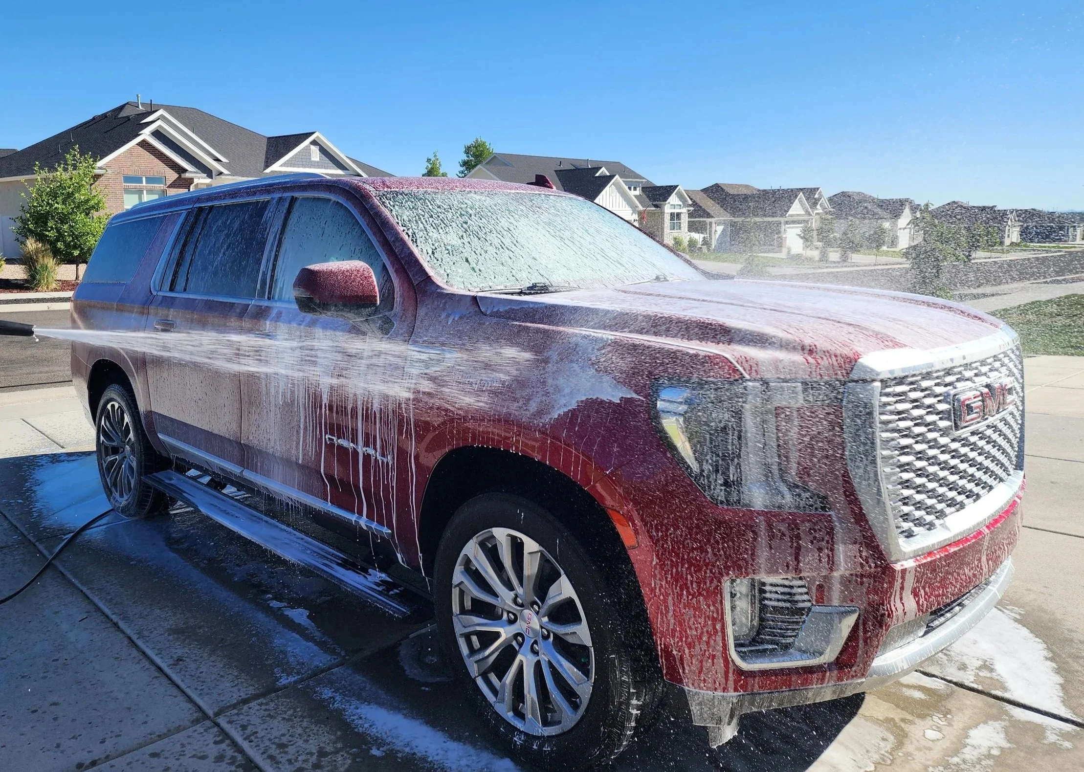 Red GMC Yukon XL Denali covered in foam during professional mobile detailing service in a Utah residential driveway — Scrub Tub car detailing