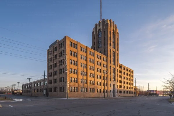 A large historic brick building with a tall tower section, located at a street corner under a clear sky.