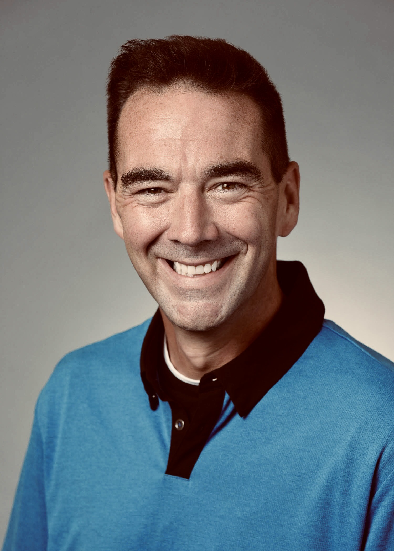 Smiling man with short dark hair, wearing a dark jacket, in black-and-white photo.