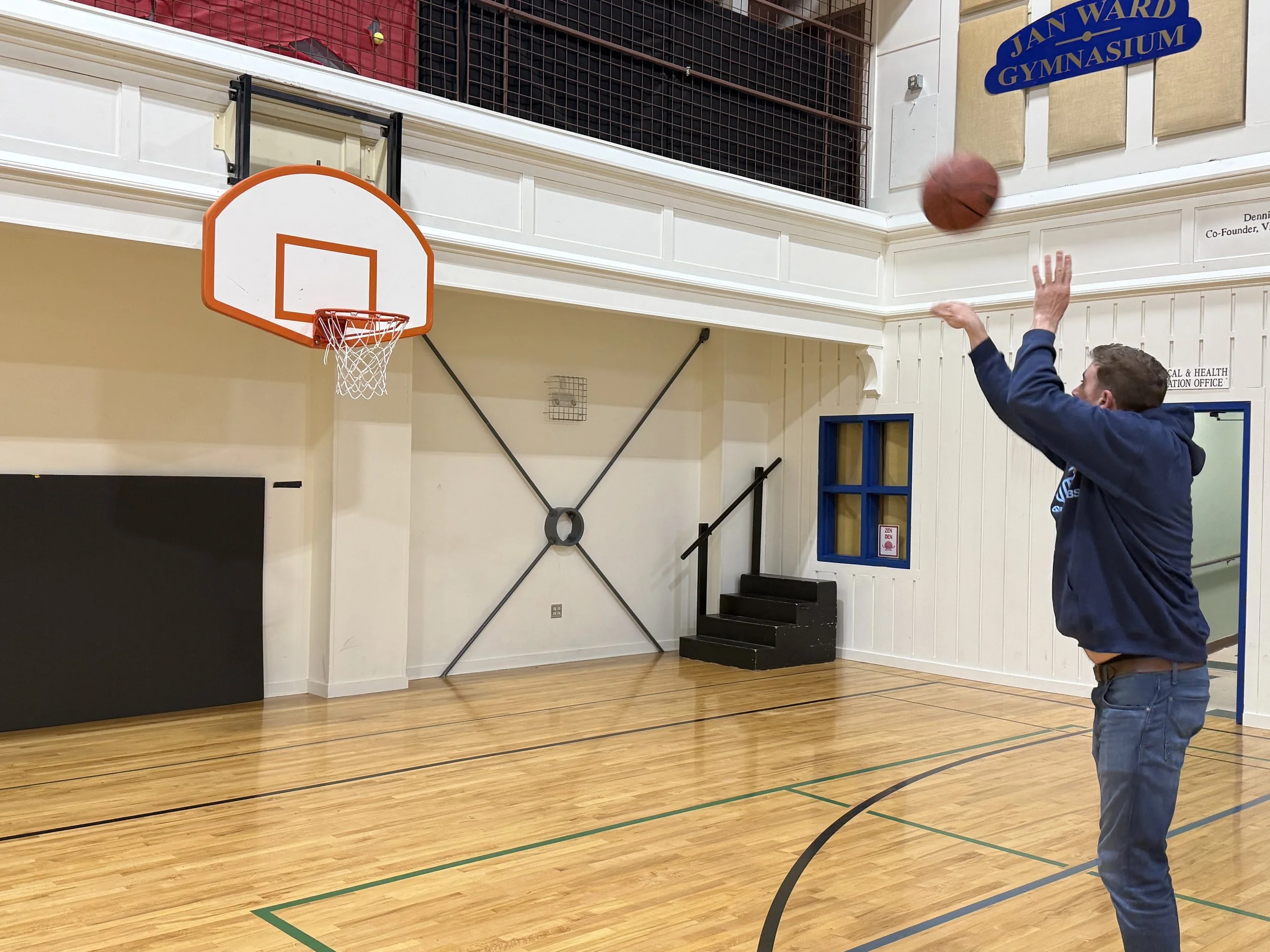 Person shooting a basketball towards the hoop in a gymnasium.