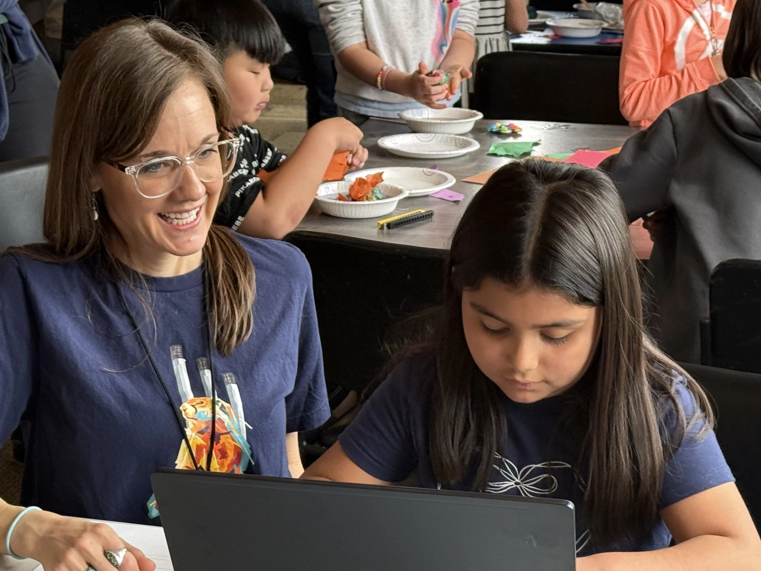People gathered at a table engaging in a hands-on activity, with some holding colorful materials and others working or observing.