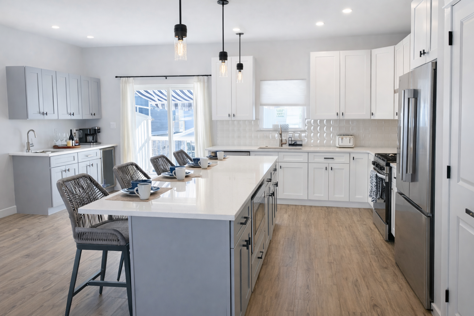 Modern kitchen with white cabinets, a large central island, stainless steel appliances, and wood flooring. Four chairs are set around the island with cups and plates.