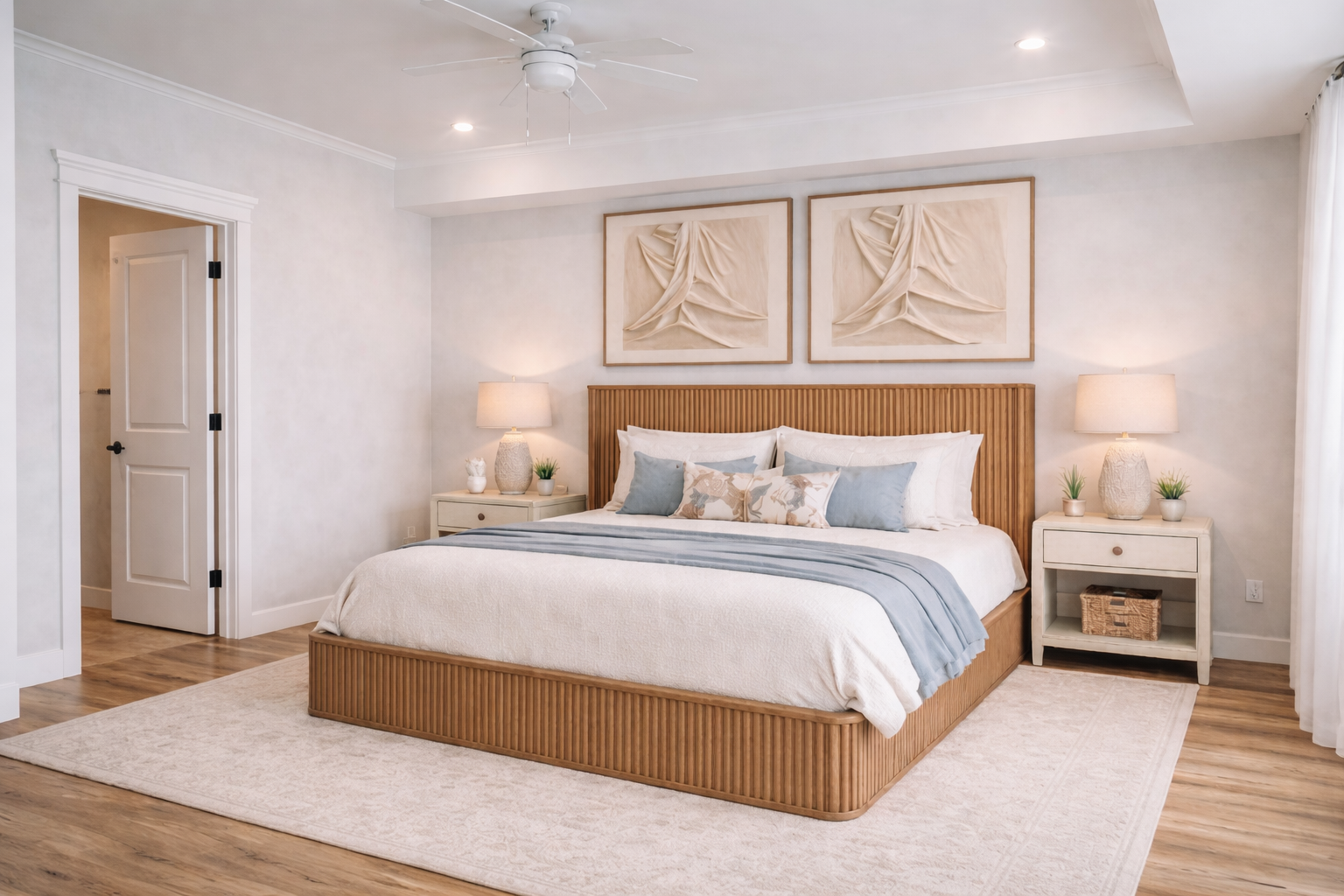 A bedroom with a wooden bed frame, white bedding, and decorative pillows. Two white nightstands with lamps and decor. Wall art above the bed. A light-colored rug on wooden floor. Multiple ceiling lights and a ceiling fan.
