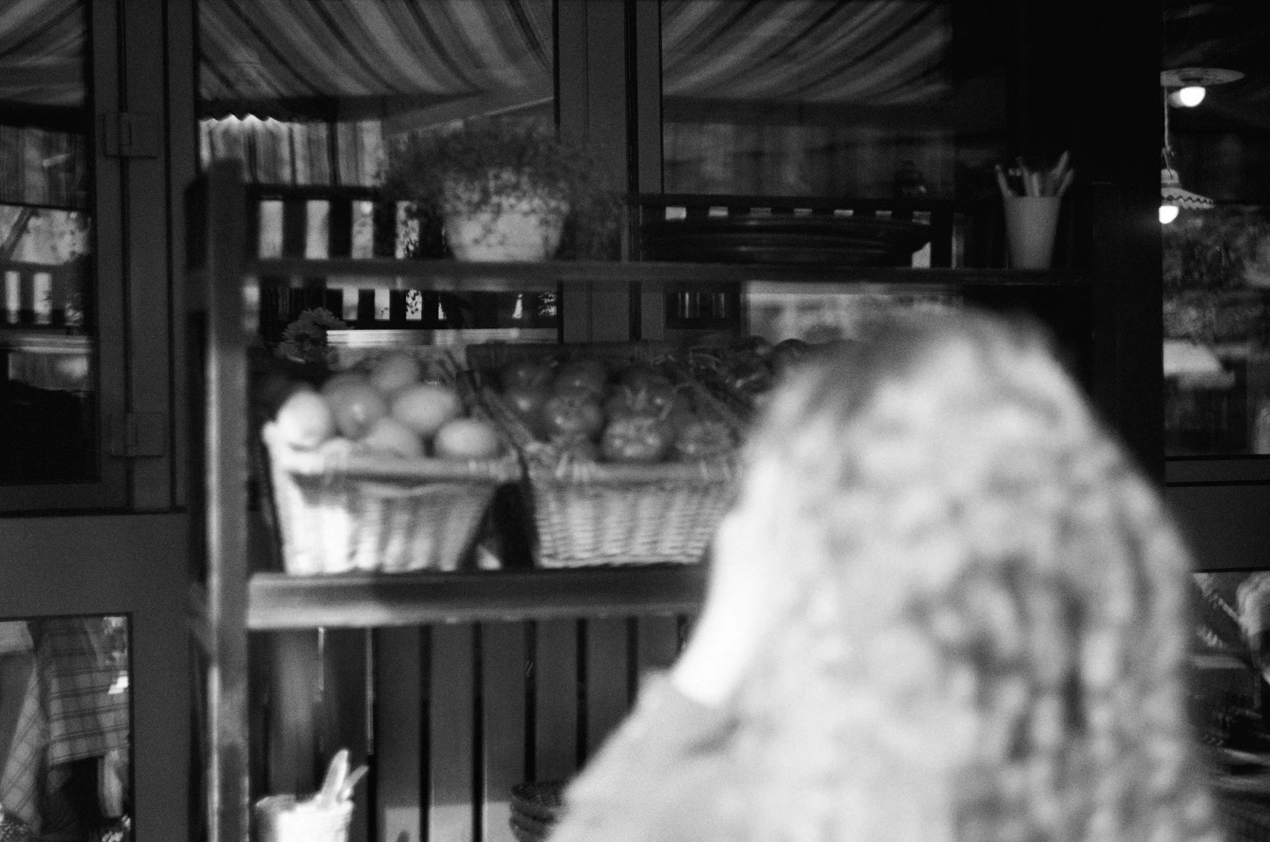 A black and white photo of a display shelf with a basket of eggs in the foreground, a potted plant, and containers holding utensils in the background.