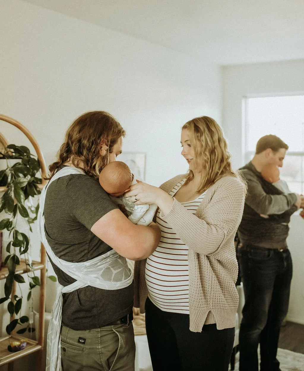 A woman in labor holding a newborn, with a man and woman standing nearby in a home setting.