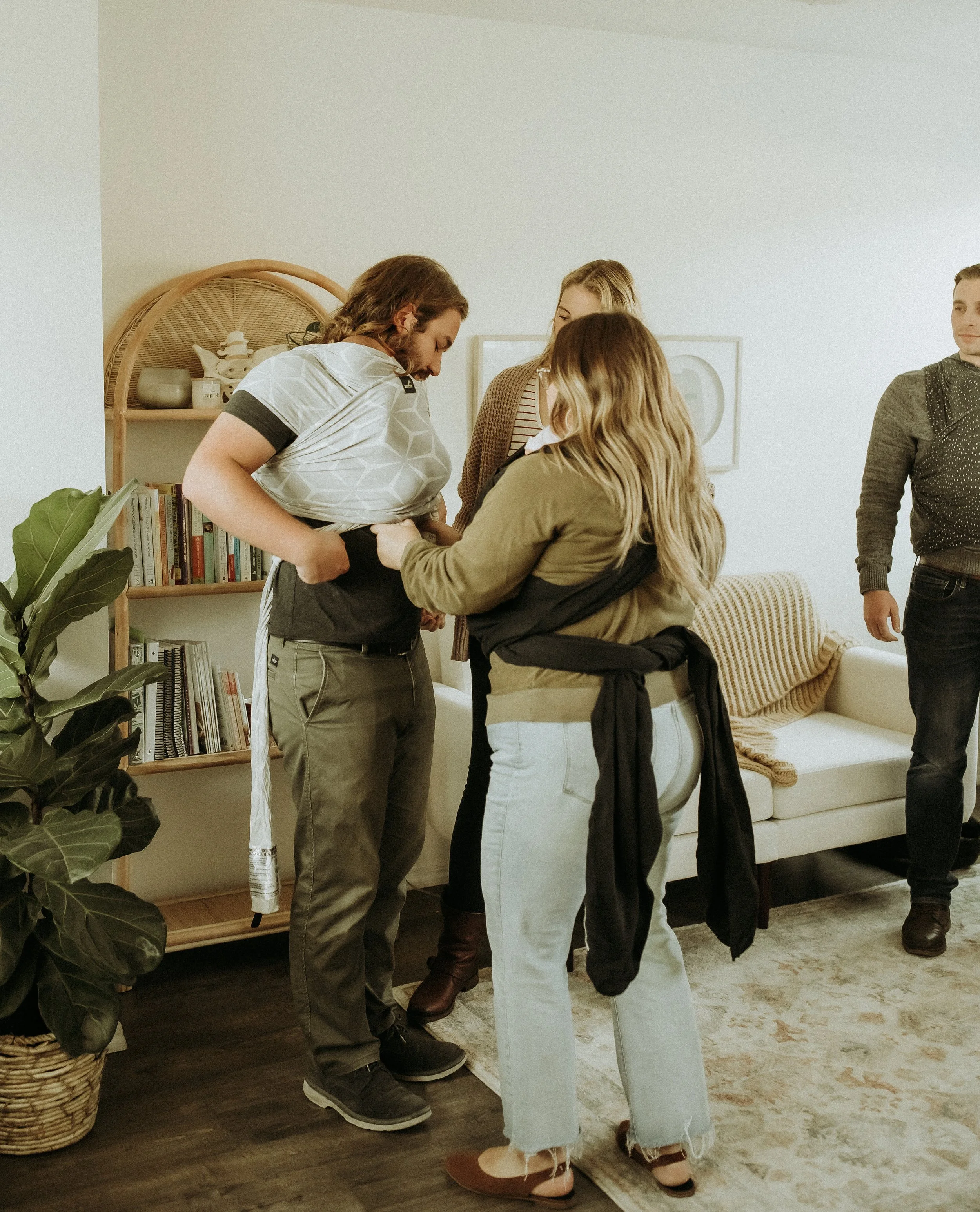 A group of five friends in a cozy living room, with two women in the foreground hugging and three people standing behind them, all engaged in a warm and friendly gathering.