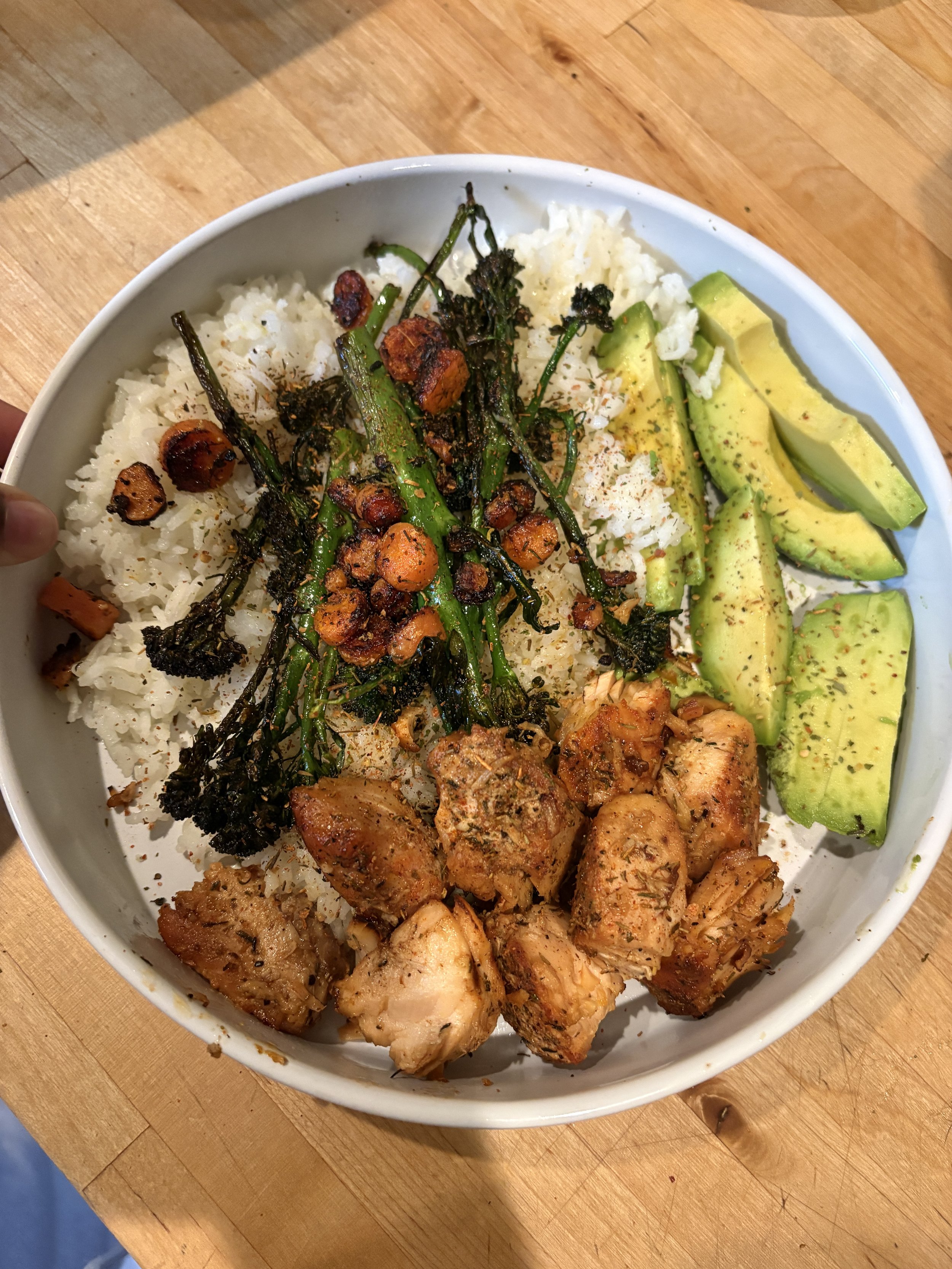 A white bowl filled with white rice, grilled vegetables, and chunks of cooked chicken on a wooden table.