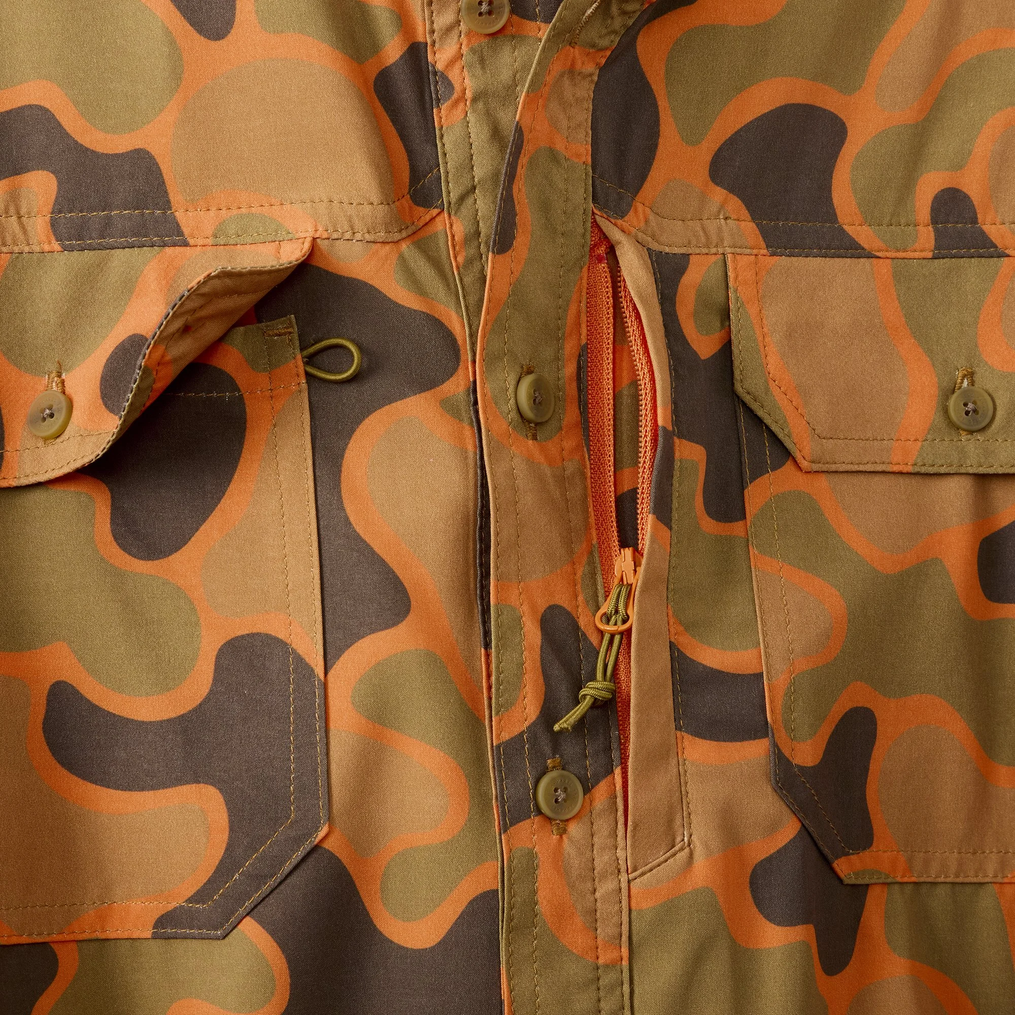 Close-up of a camouflage patterned jacket with buttons, a zipper, and a pocket.