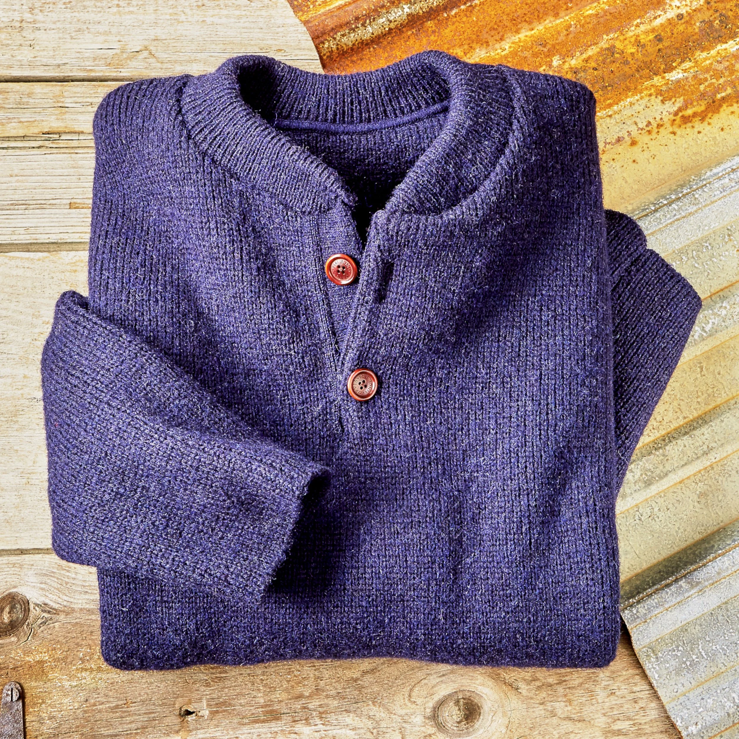 A folded purple knitted sweater with red buttons on front, resting on a weathered wooden surface and partially covering a striped cloth.
