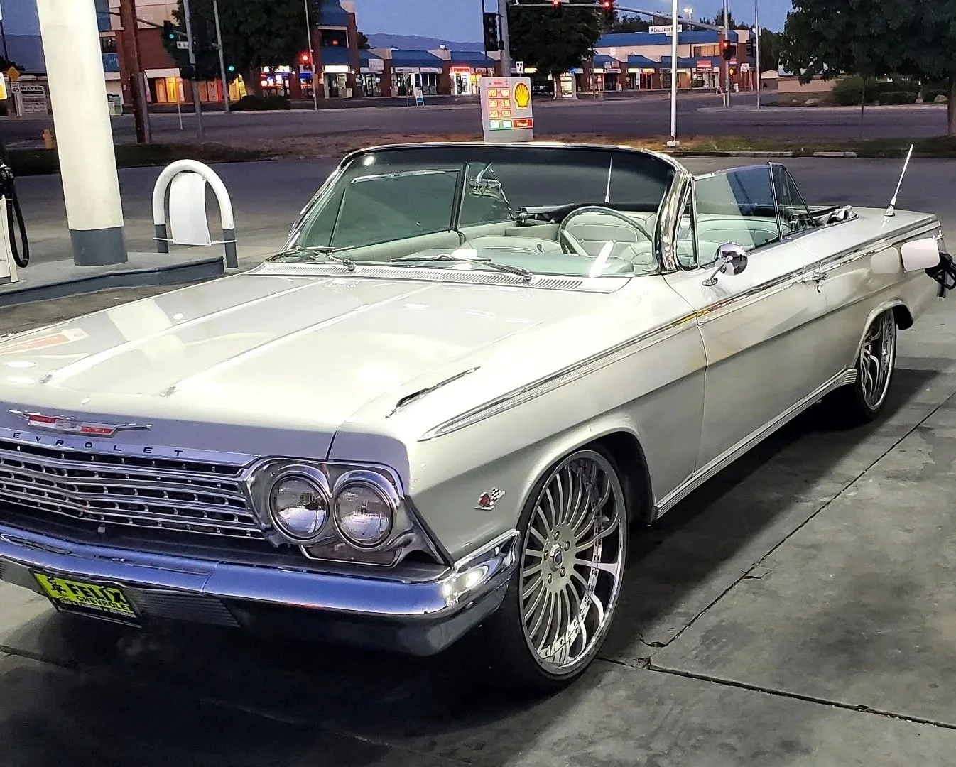 A vintage silver Chevrolet convertible car parked at a gas station evening.
