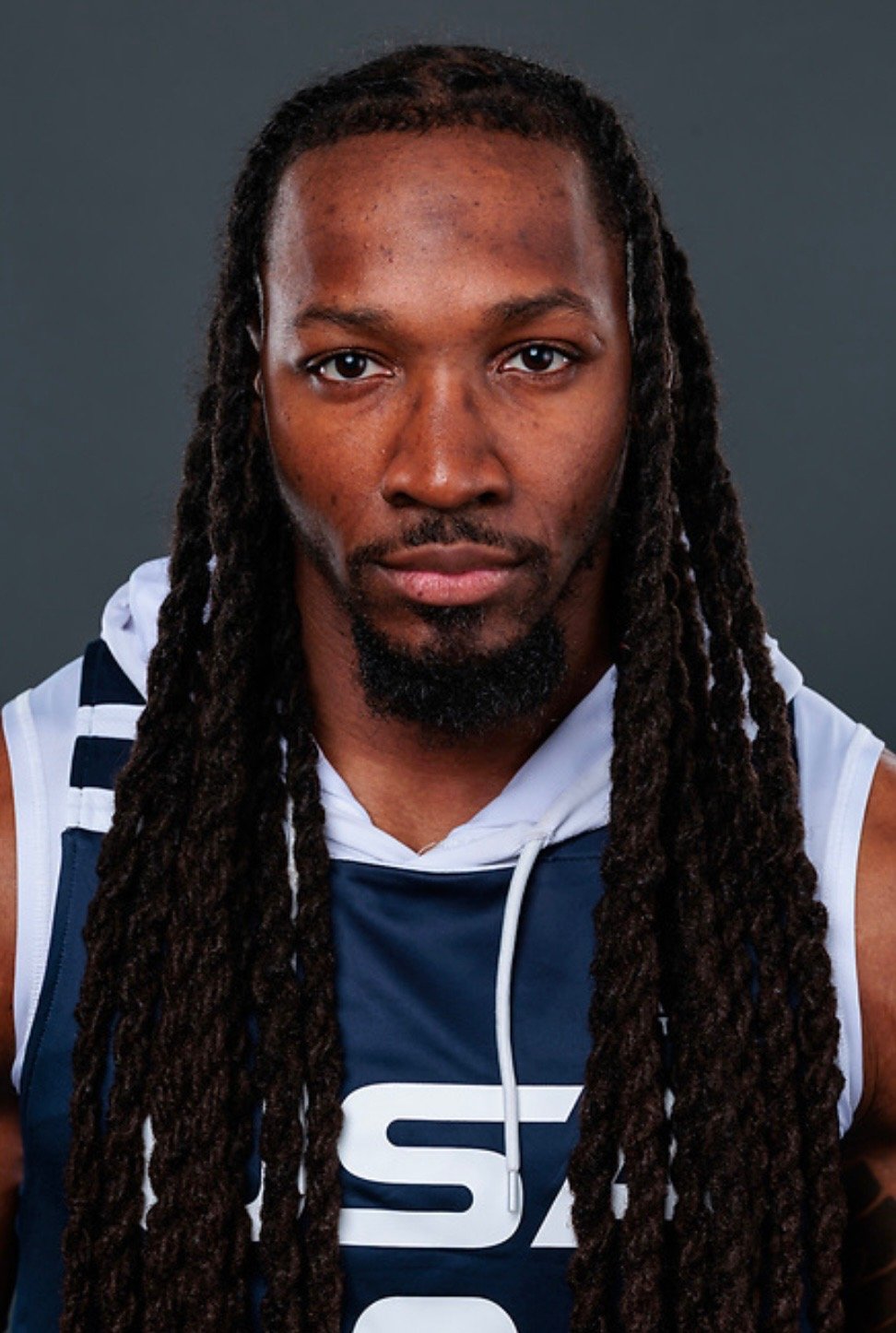 Portrait of a man with long dreadlocks wearing a sports jersey and looking directly at the camera.