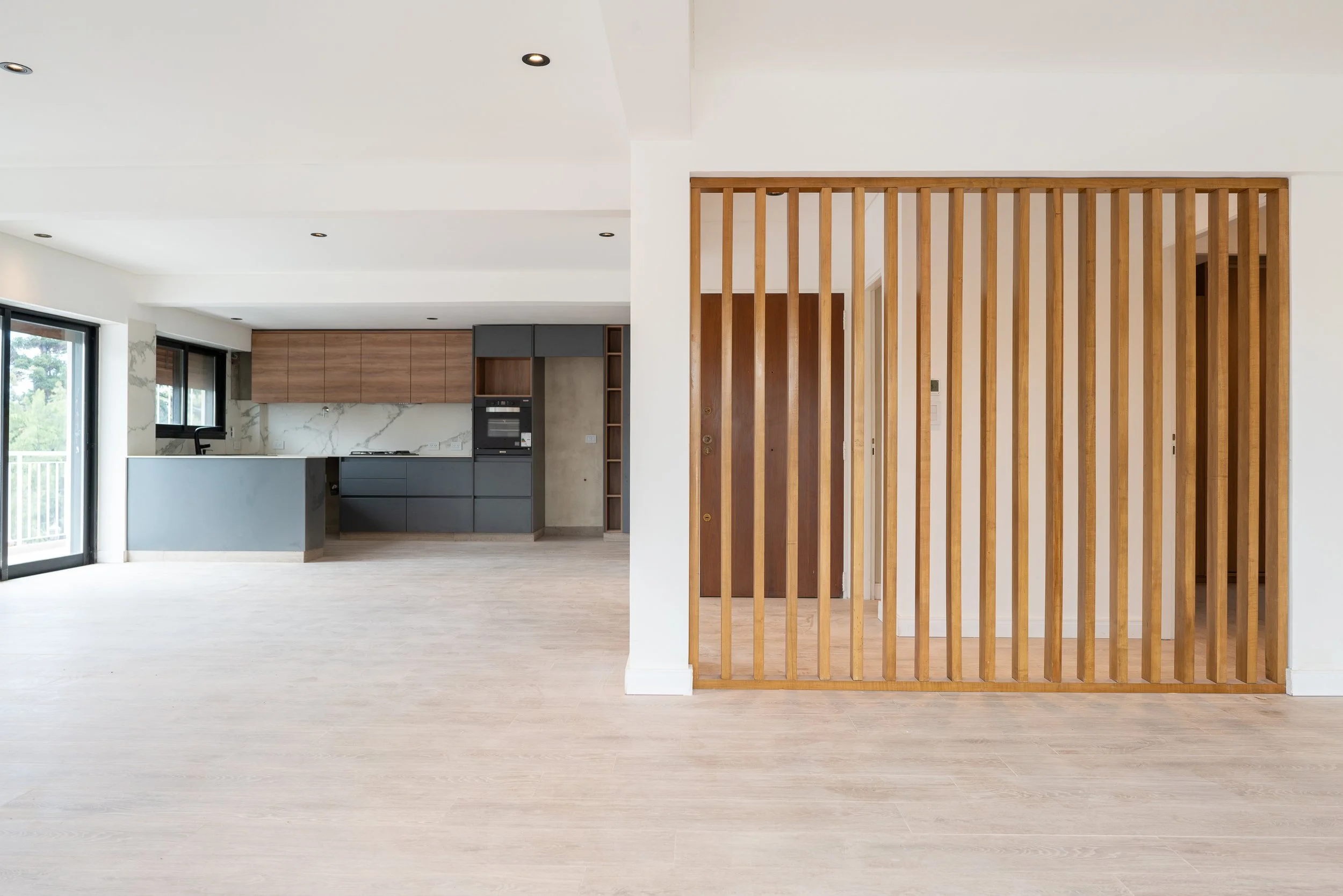 Interiores de una casa moderna con cocina y espacio vacío, separado por una estructura de listones de madera.