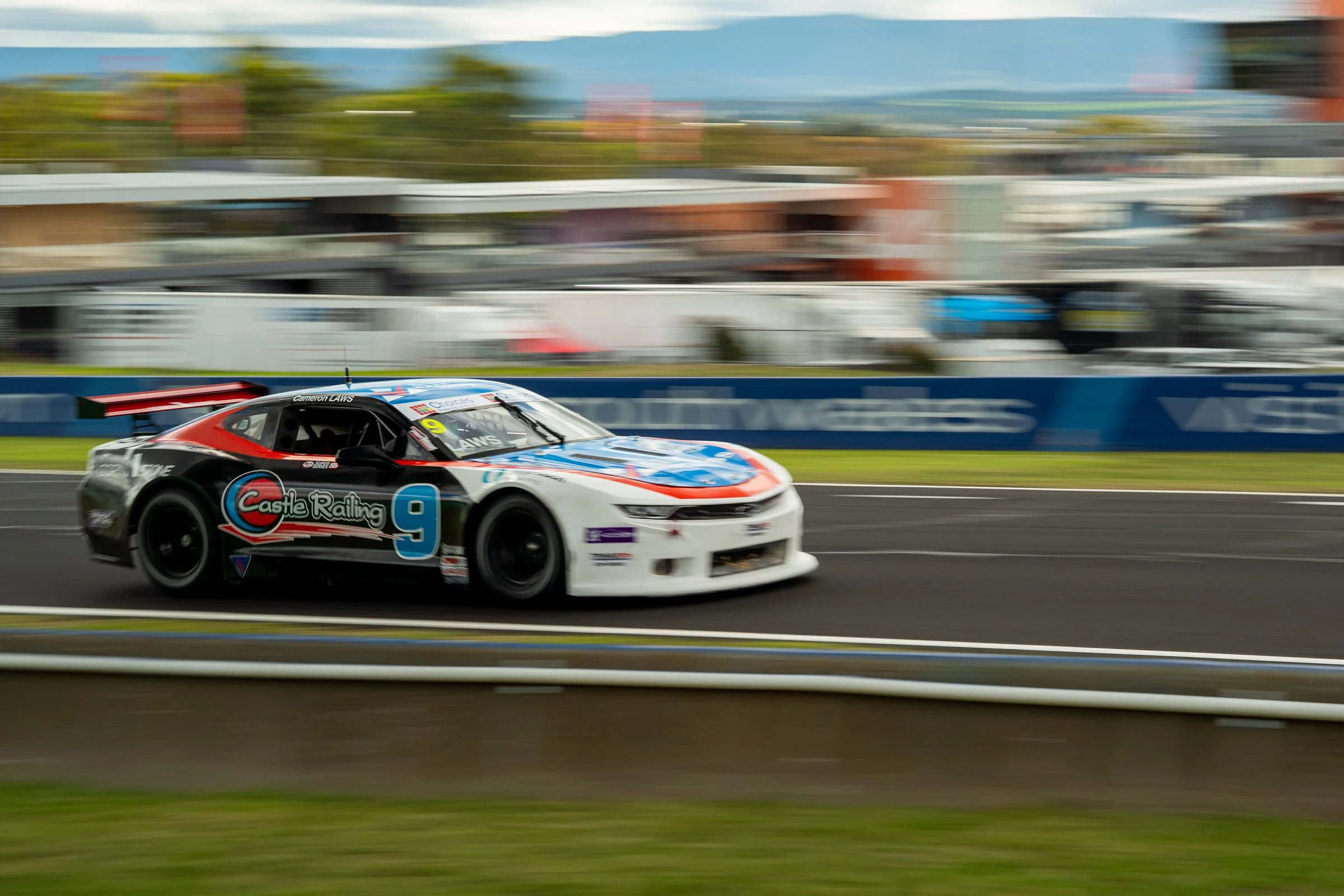 Blue, red and white Chevrolet race car number 9 speeding on track with the background blurred by motion